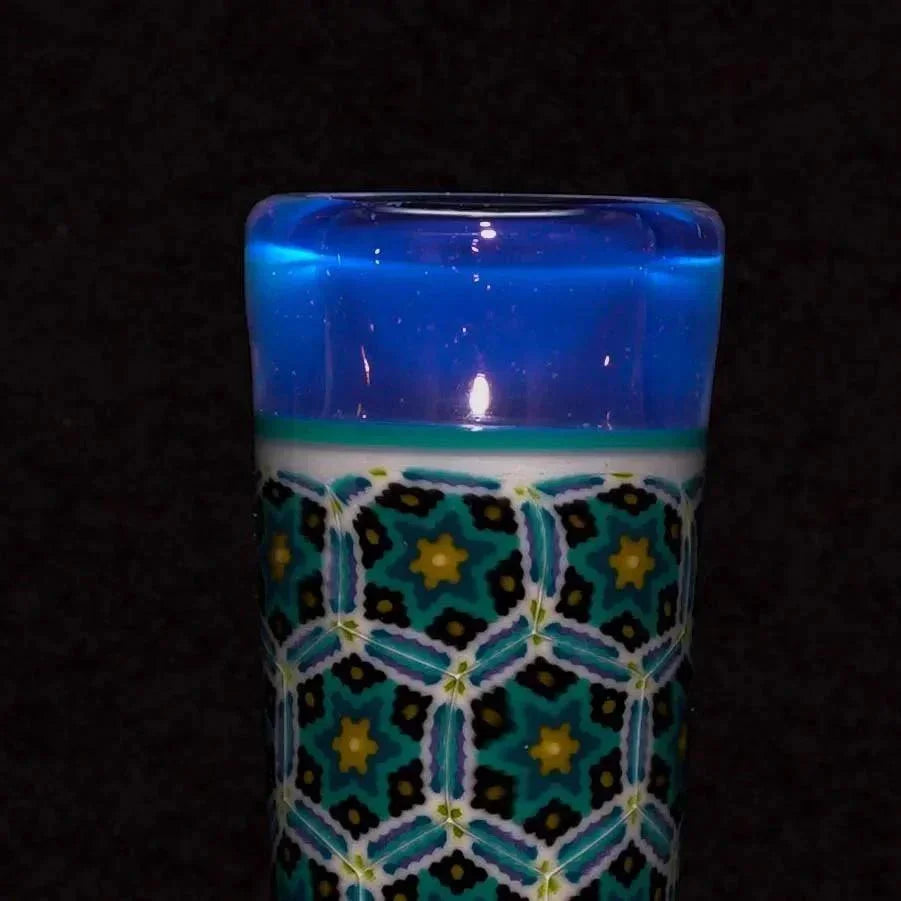 Close-up of a patterned glass tube with blue rim and geometric mosaic design