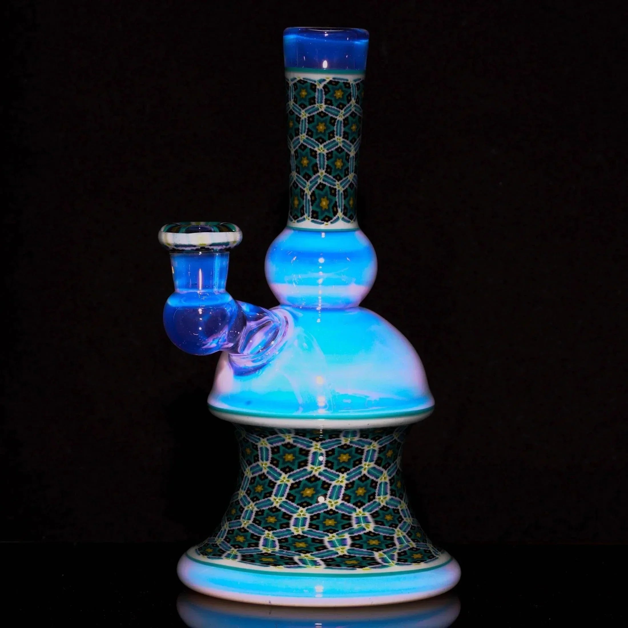 Intricate blue and patterned heady glass water pipe with geometric mosaic design on black background.