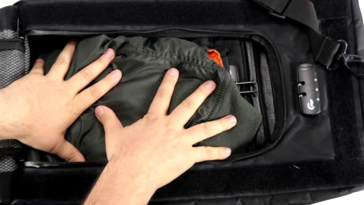 Hands packing clothing into a black smell proof bag with lock and shoulder strap