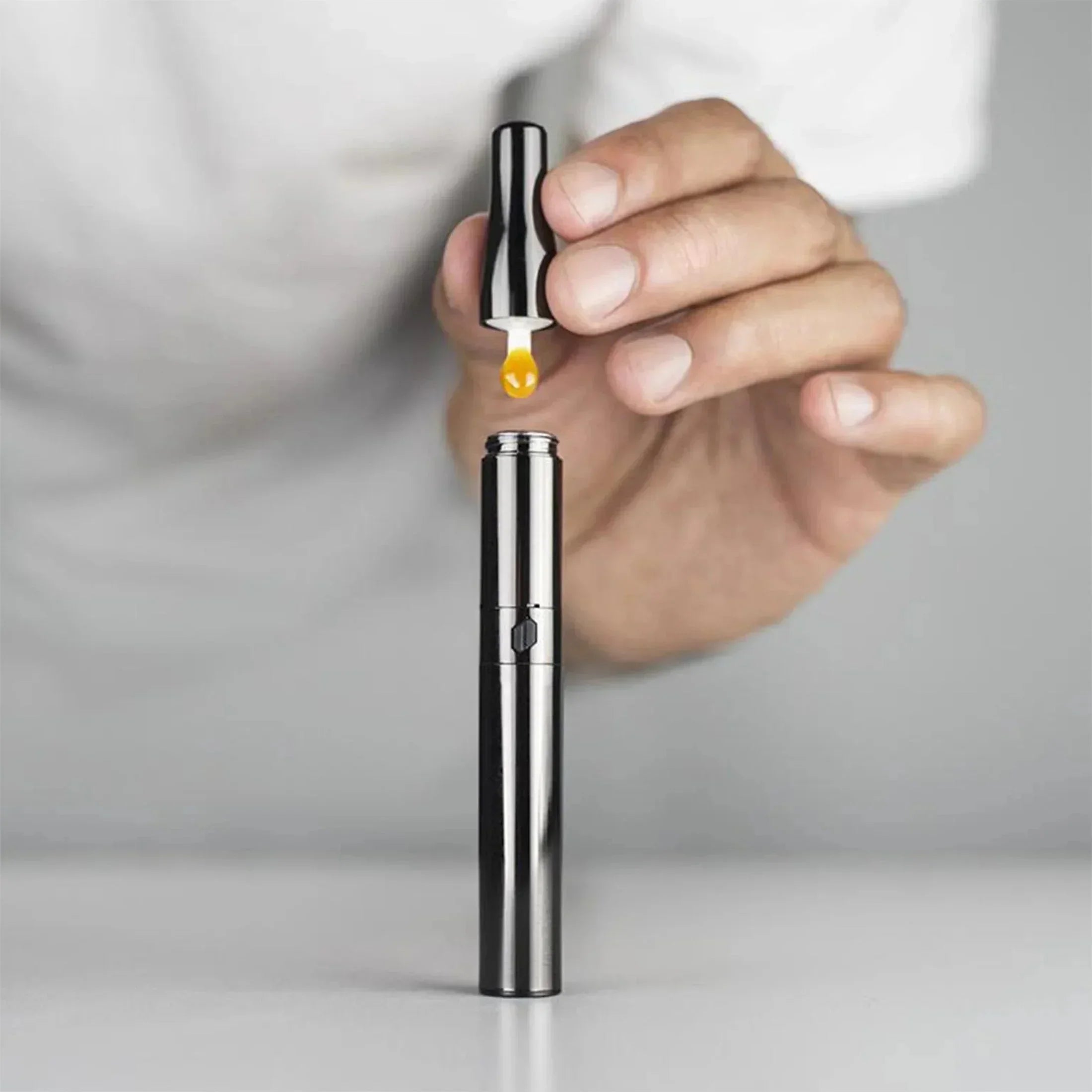 Hand loading concentrate into a sleek metal vaporizer pen on a white surface.