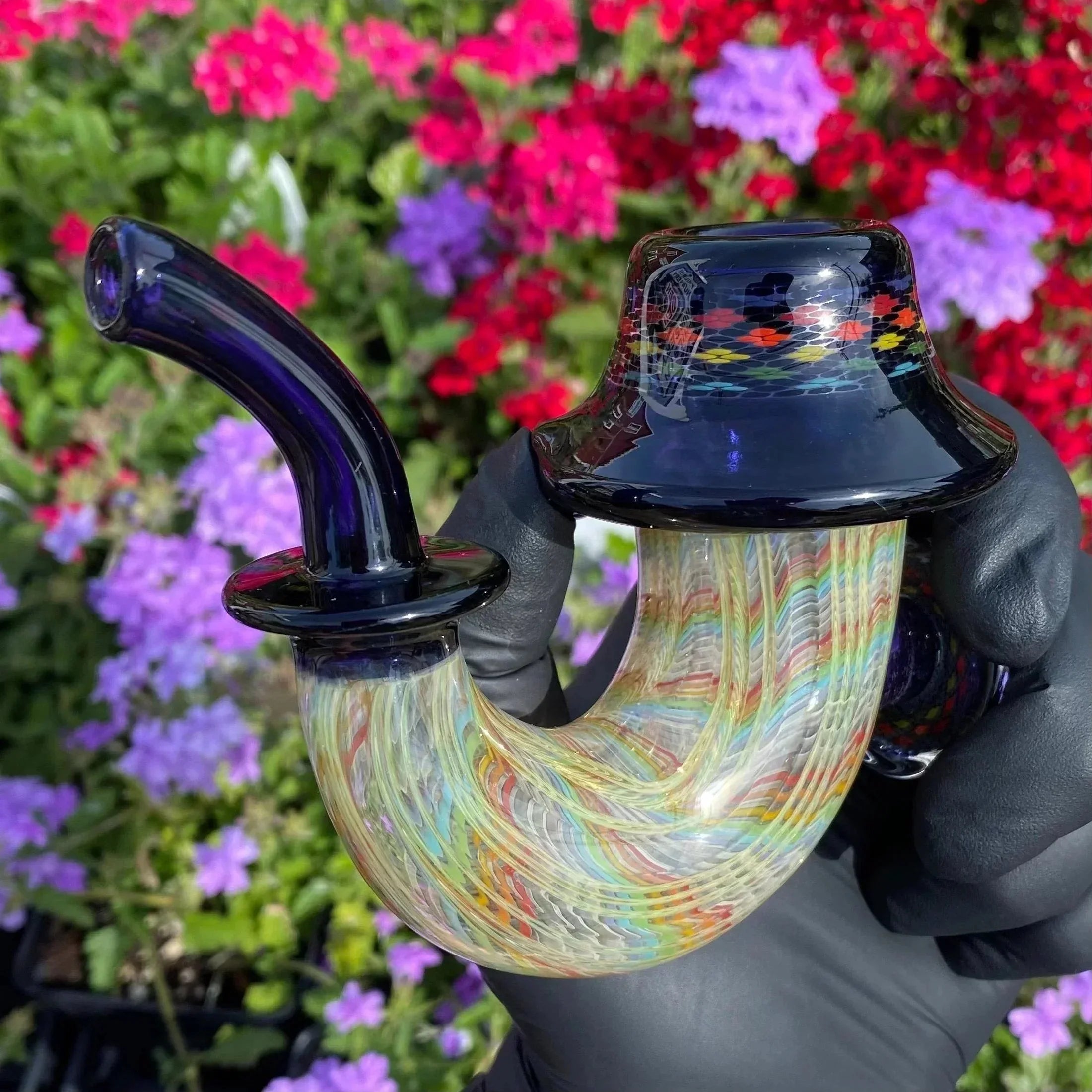 Colorful heady glass pipe with intricate patterns, held by gloved hand, floral background