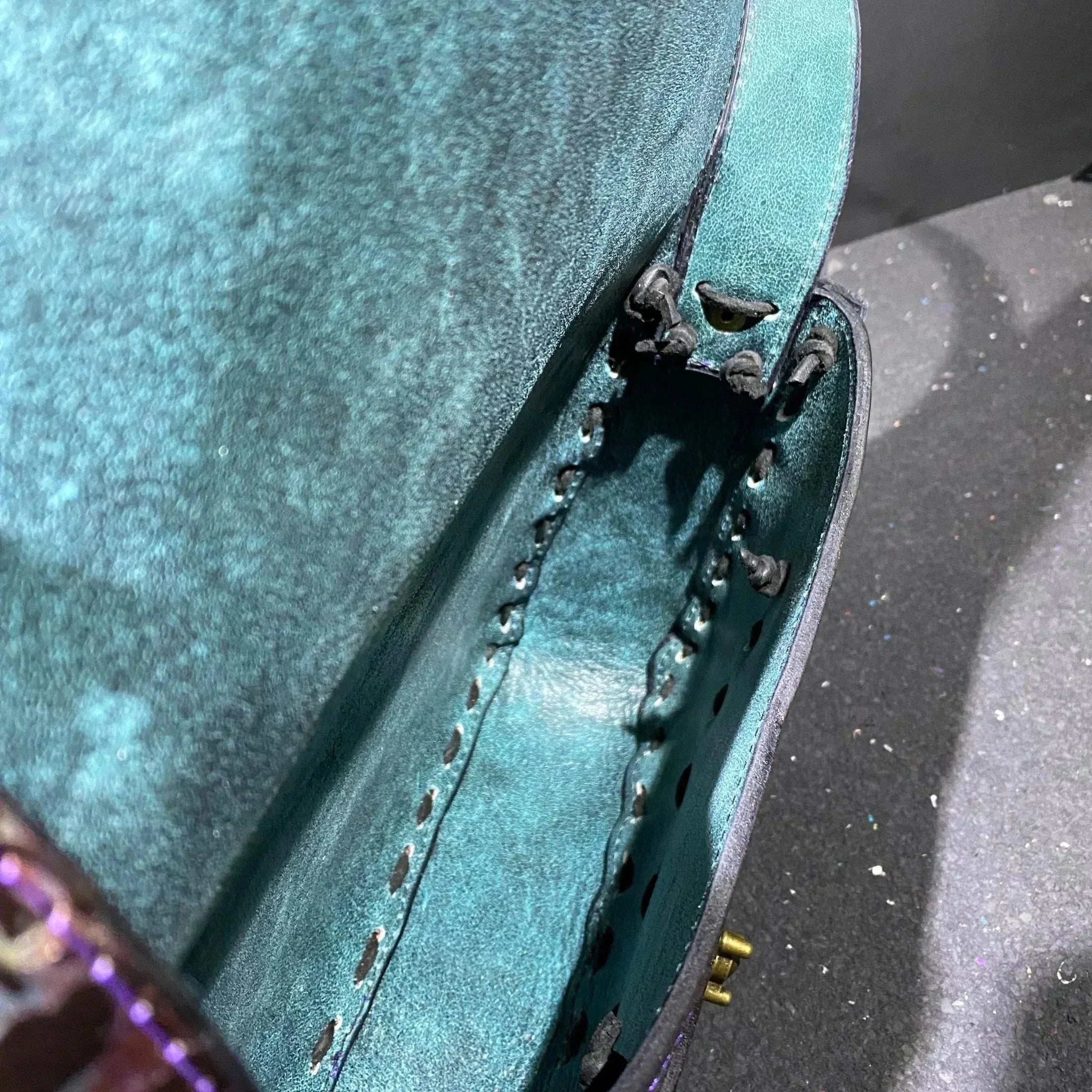 Close-up of turquoise leather bag with stitched edges and unfinished hardware