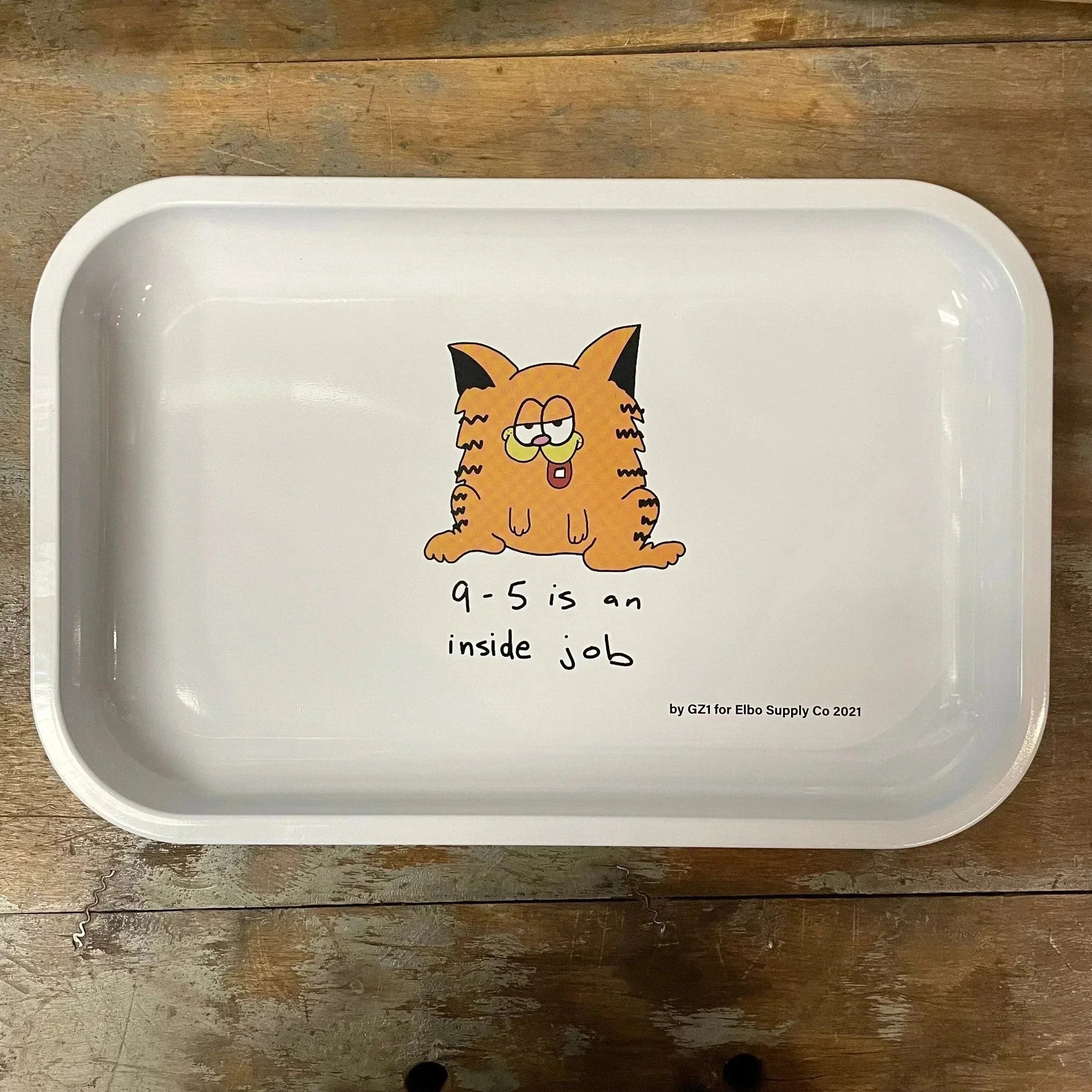 White rolling tray with cartoon orange cat and '9-5 is an inside job' text on wood surface