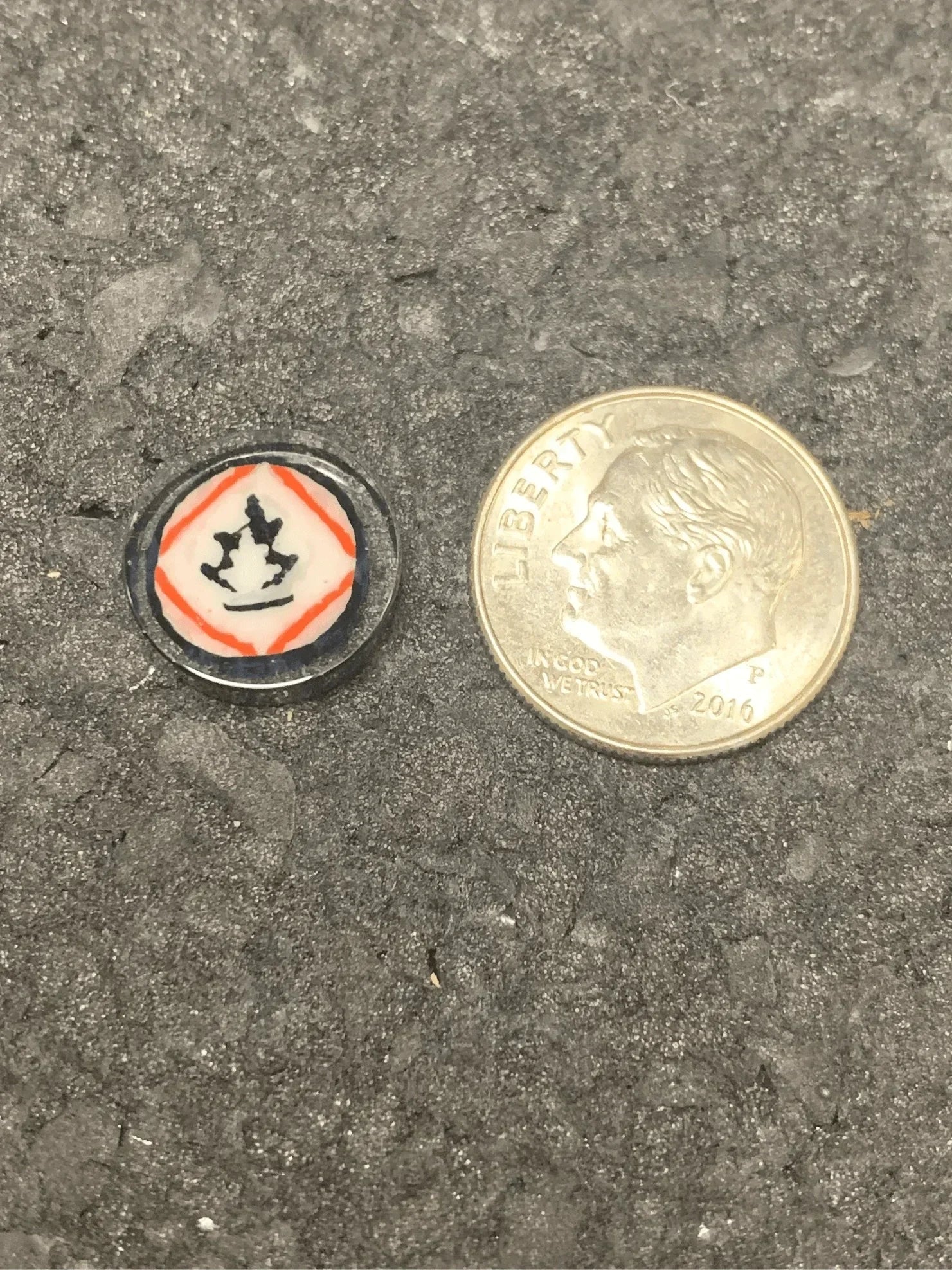 Small glass piece with orange and black design next to dime for scale, heady glass accessory