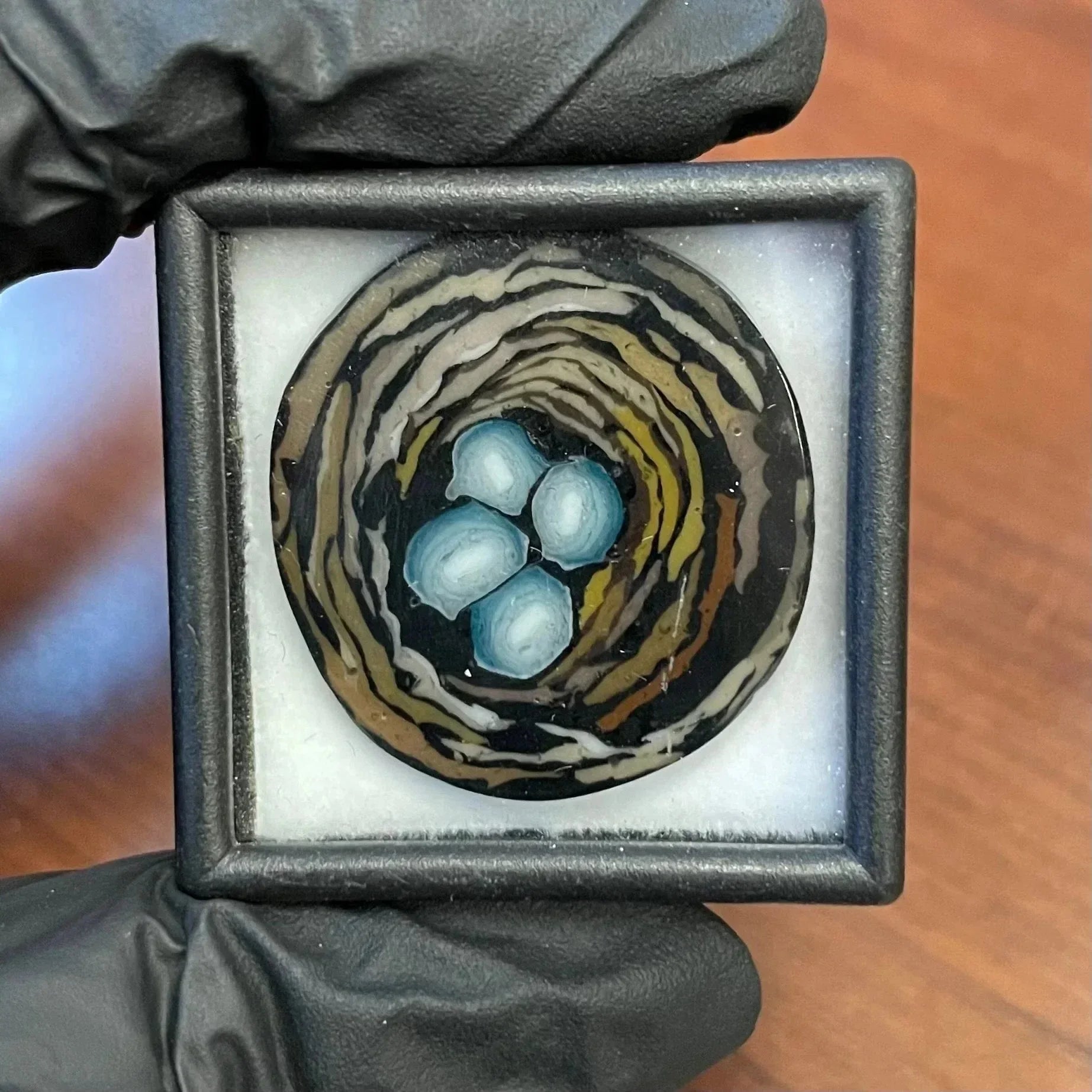 Glass art pendant featuring a bird's nest with blue eggs in a display case