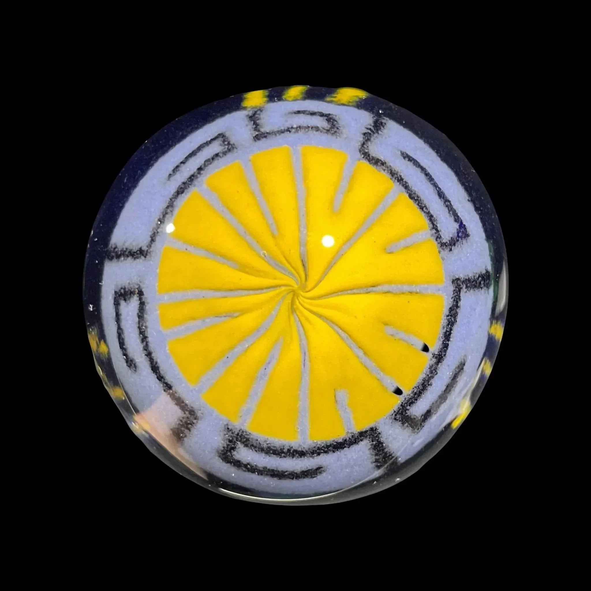 Handmade glass marble with yellow swirl and blue geometric pattern on black background