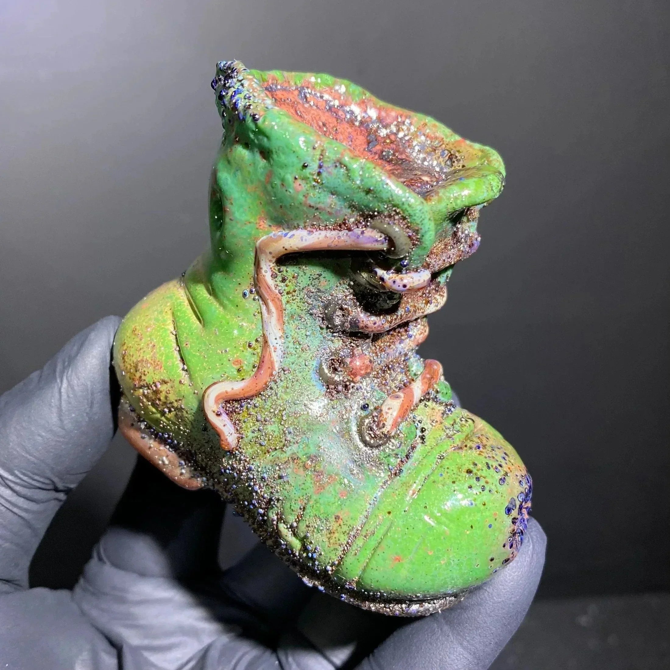 Hand holding green glass boot pipe with colorful accents and textured details