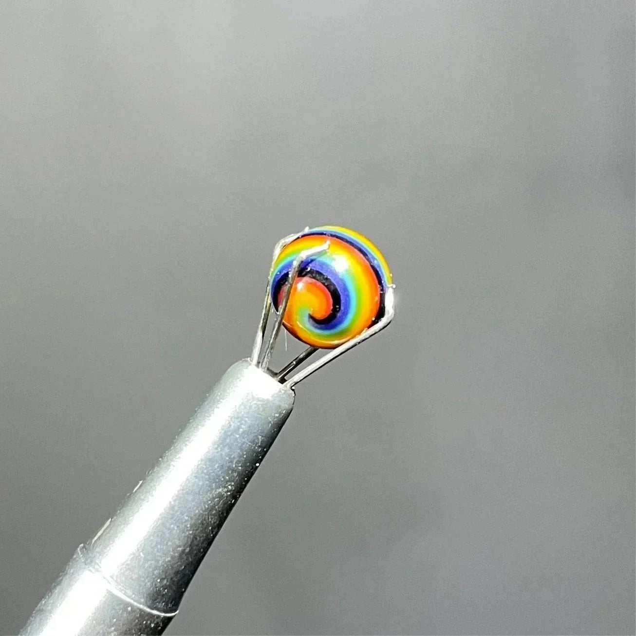 Rainbow spiral glass marble held by metal tweezers for smoking accessories