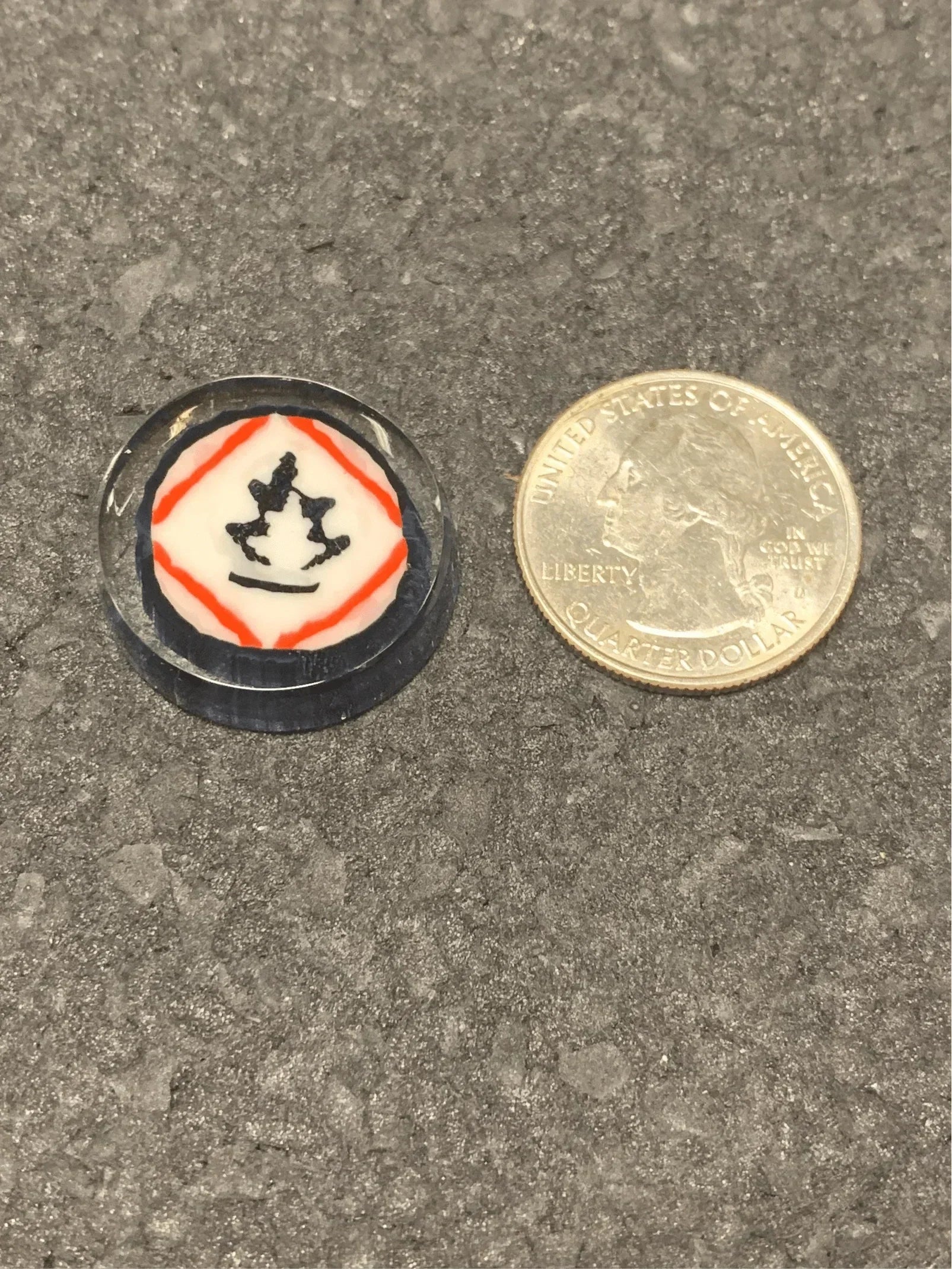 Small glass accessory with red, white, and black design next to quarter for scale