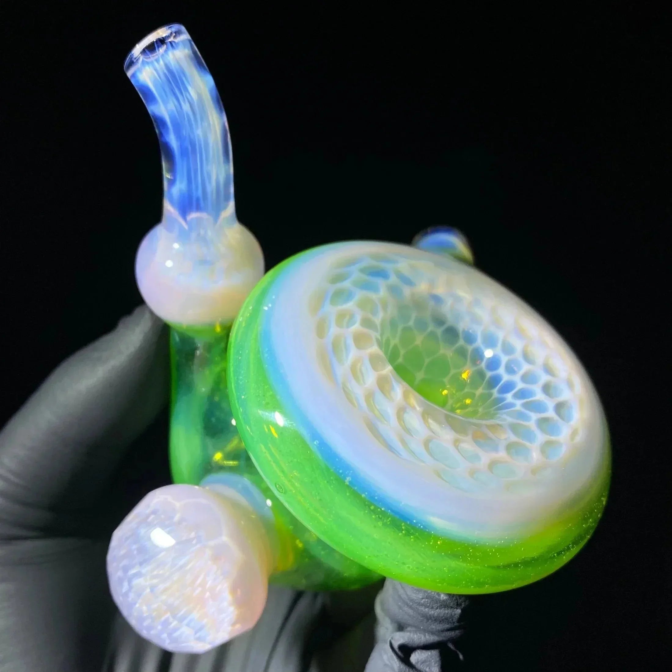 Handcrafted green and white glass pipe with honeycomb design, held with a gloved hand