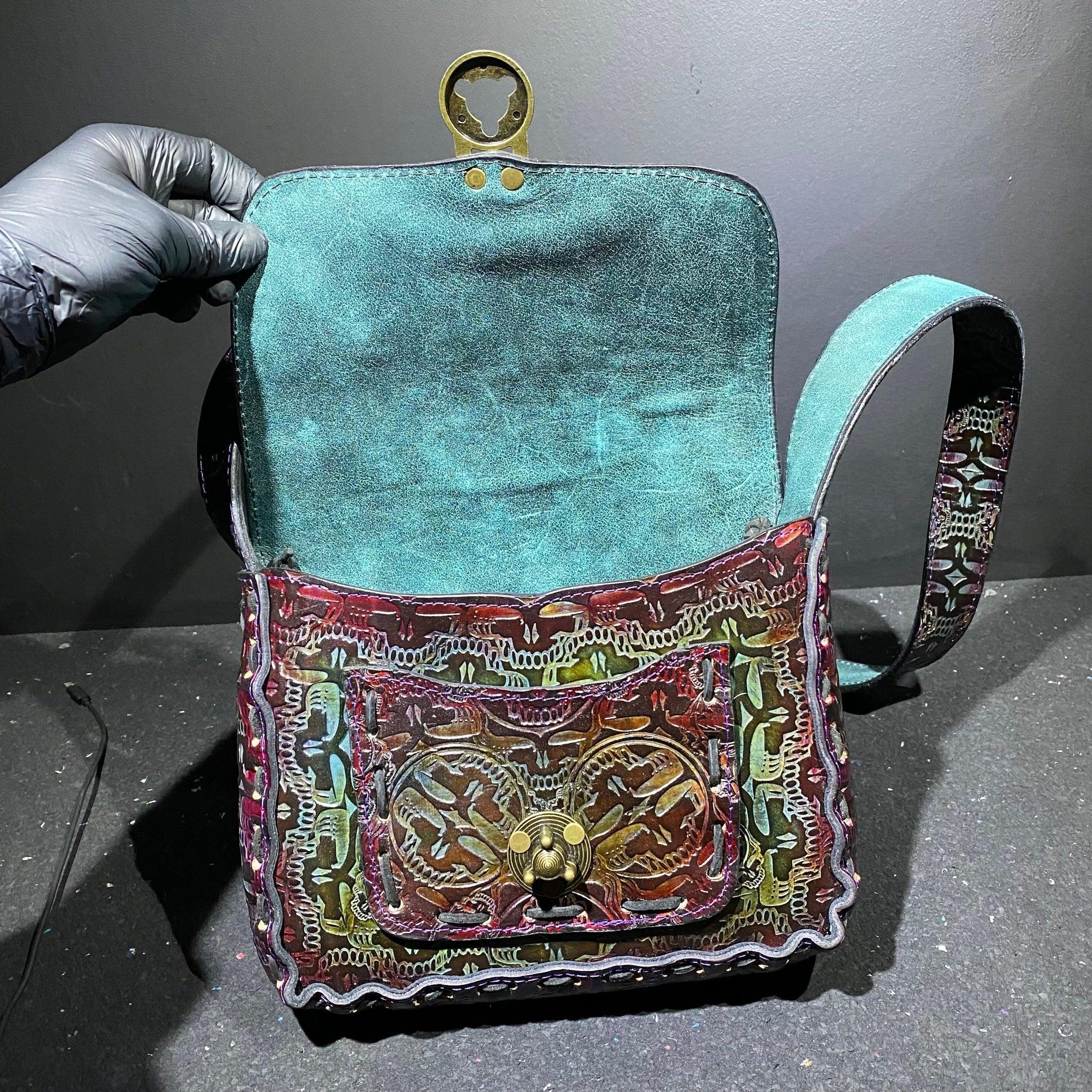 Handcrafted leather shoulder bag with intricate embossed patterns, open to show teal suede interior.
