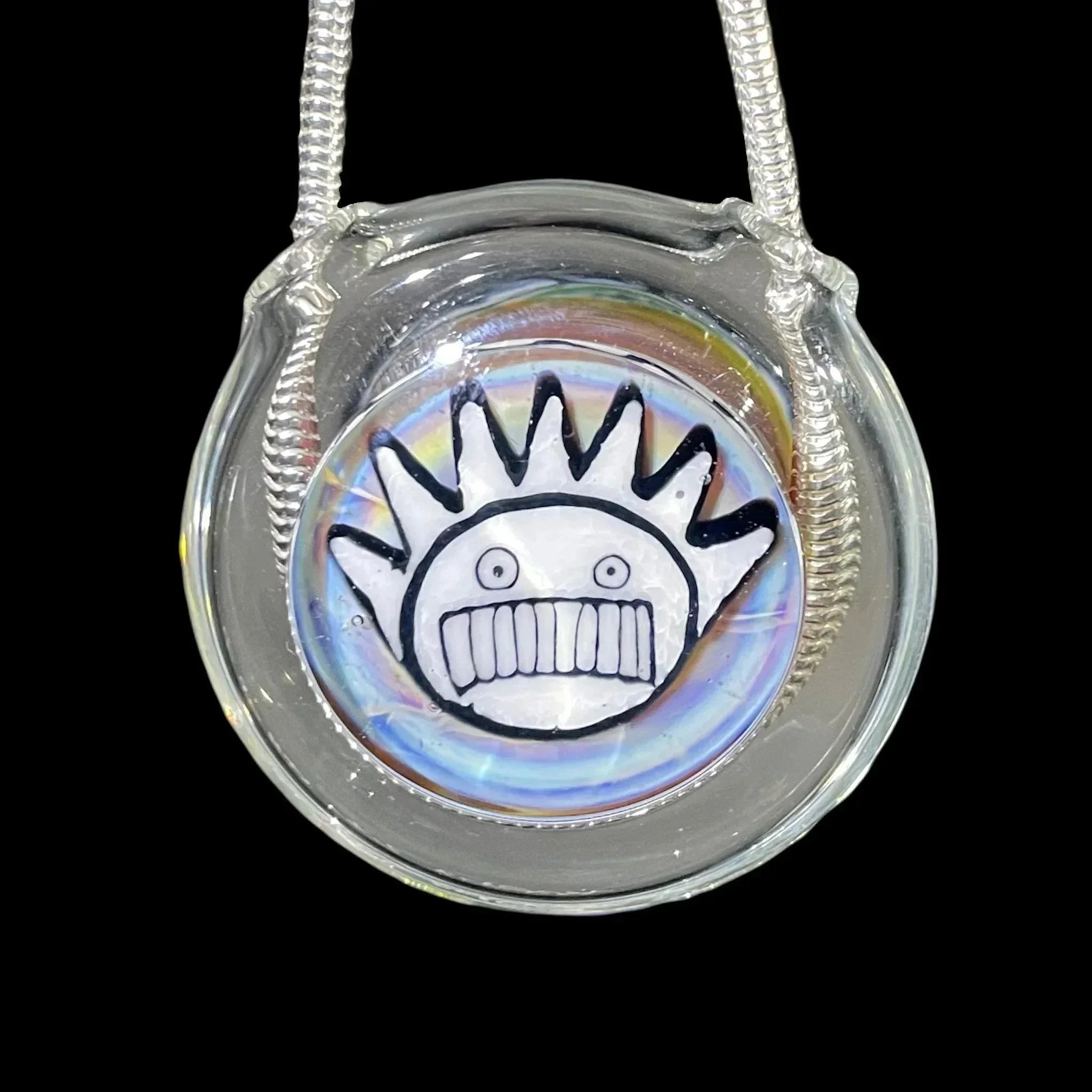 Handmade glass pendant with a smiling spiked face design and rainbow accents on a cord
