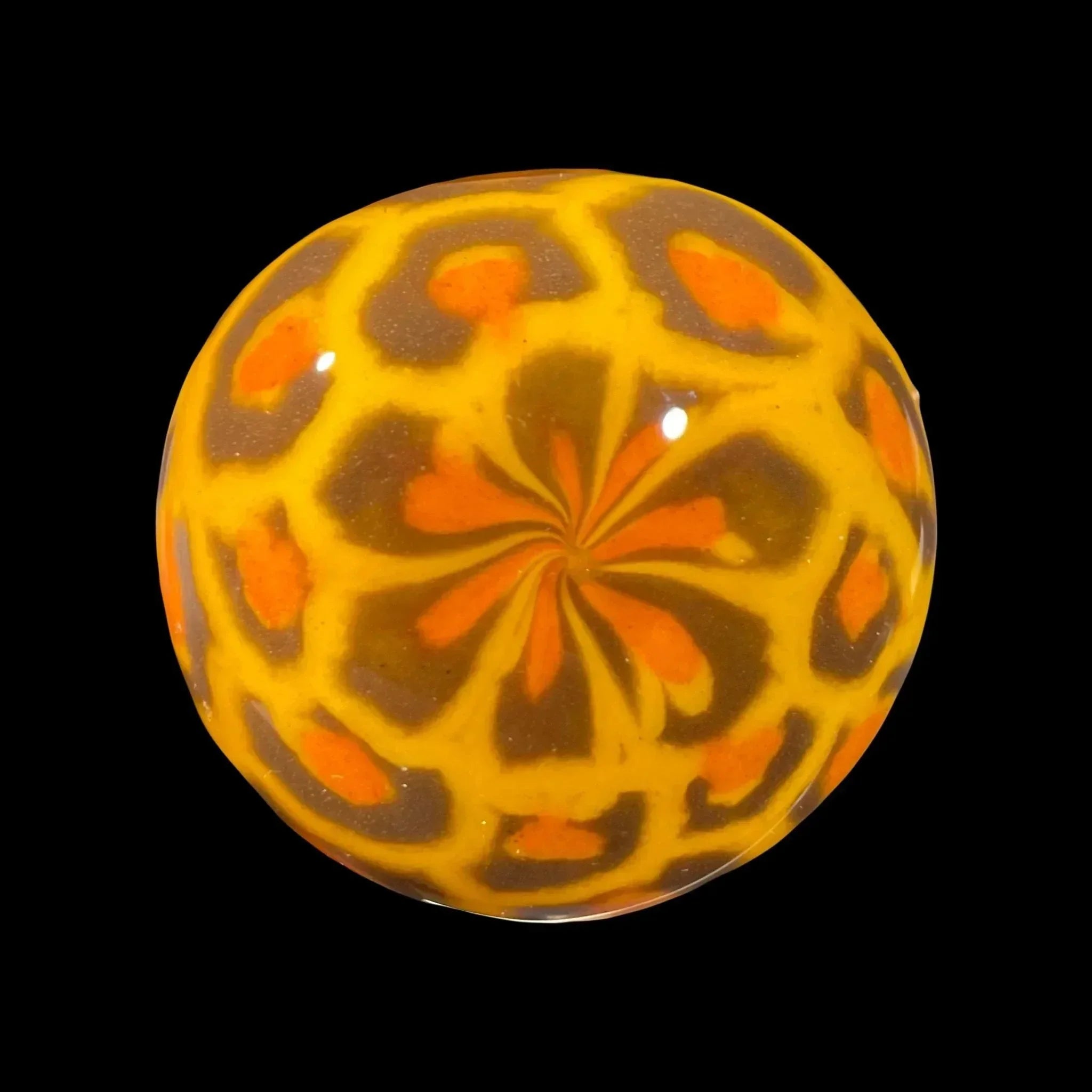 Handcrafted glass marble with orange and yellow swirl pattern on black background