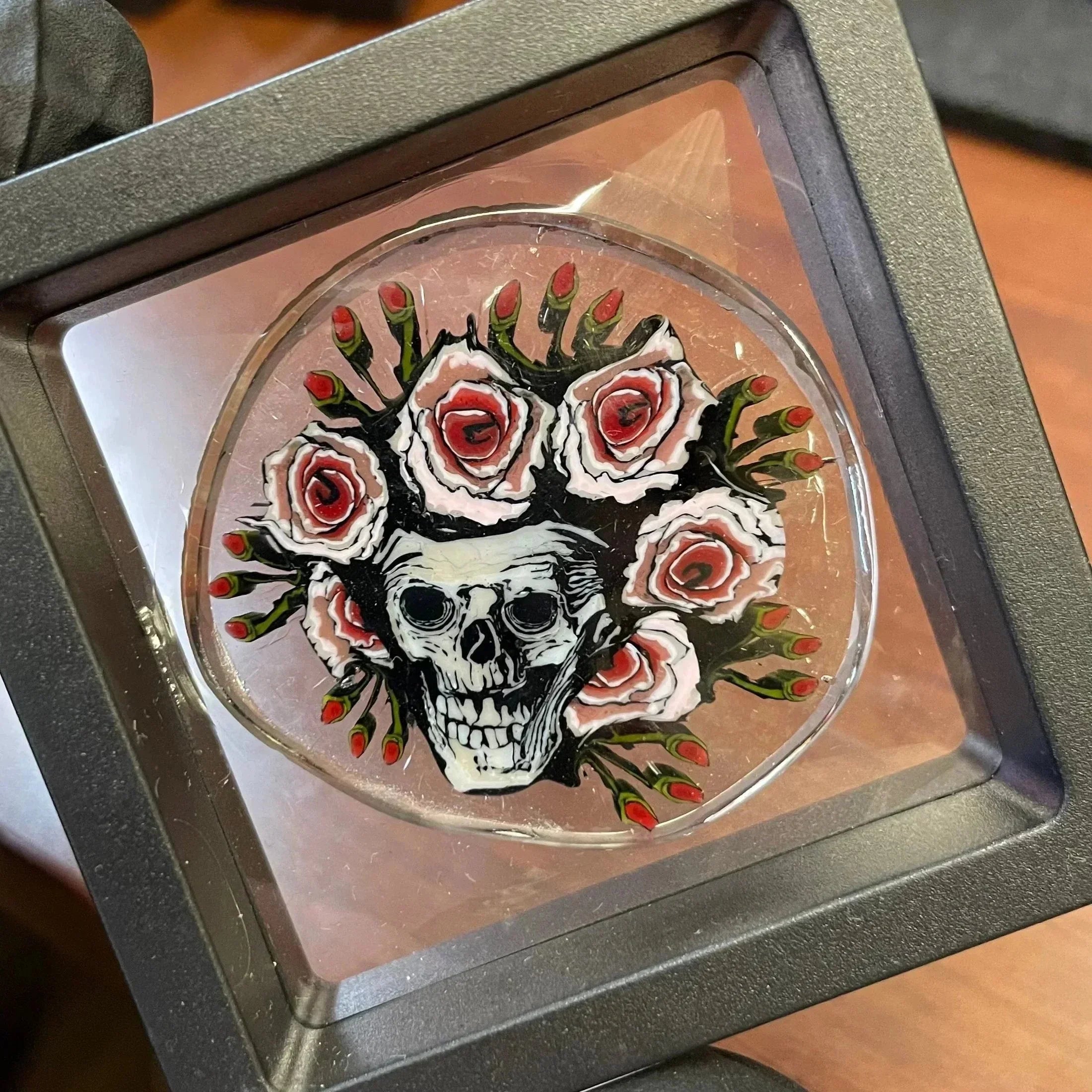 Glass art coin with skull and rose design displayed in protective case