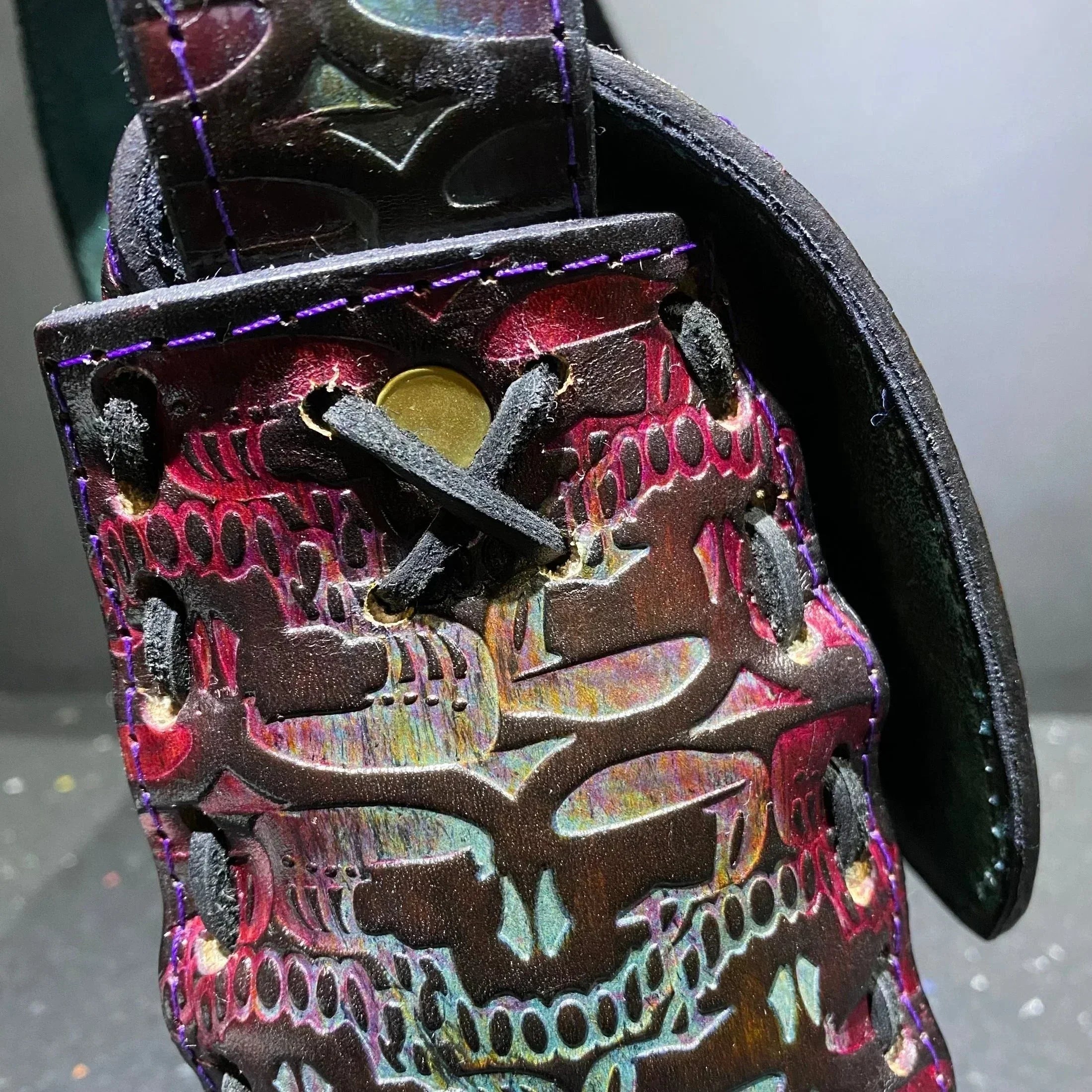 Close-up of iridescent carved leather pouch with black lacing and brass rivet detail