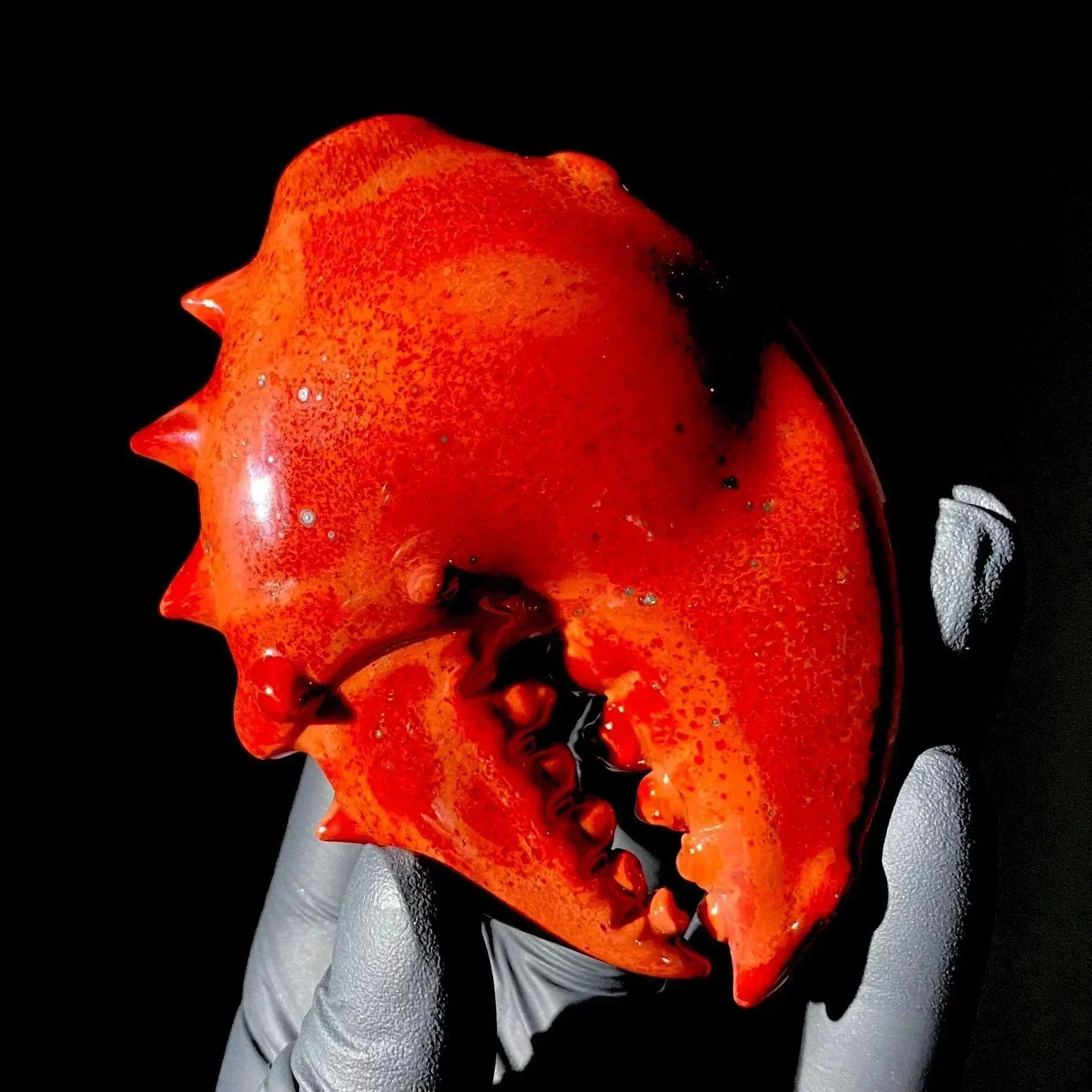 Hand holding a detailed glass crab claw sculpture with vivid red color and spiked texture