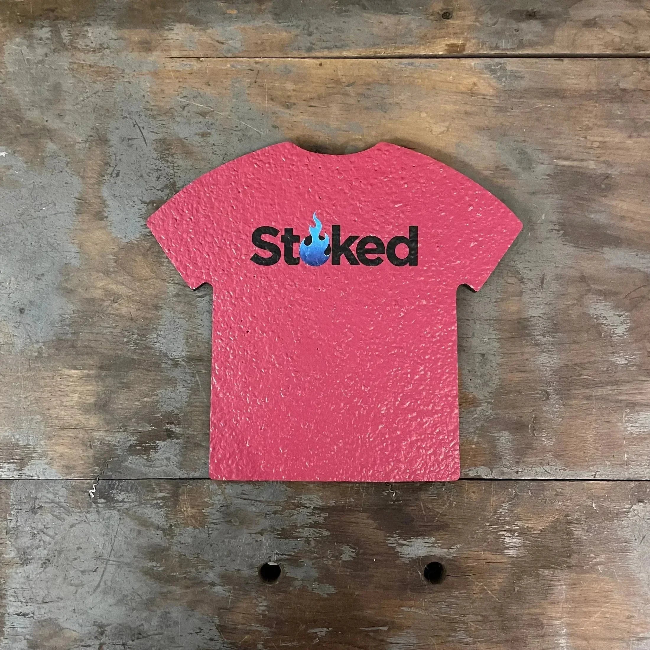 Red t-shirt-shaped dab mat with 'Stoked' and a blue flame logo on rustic wood background