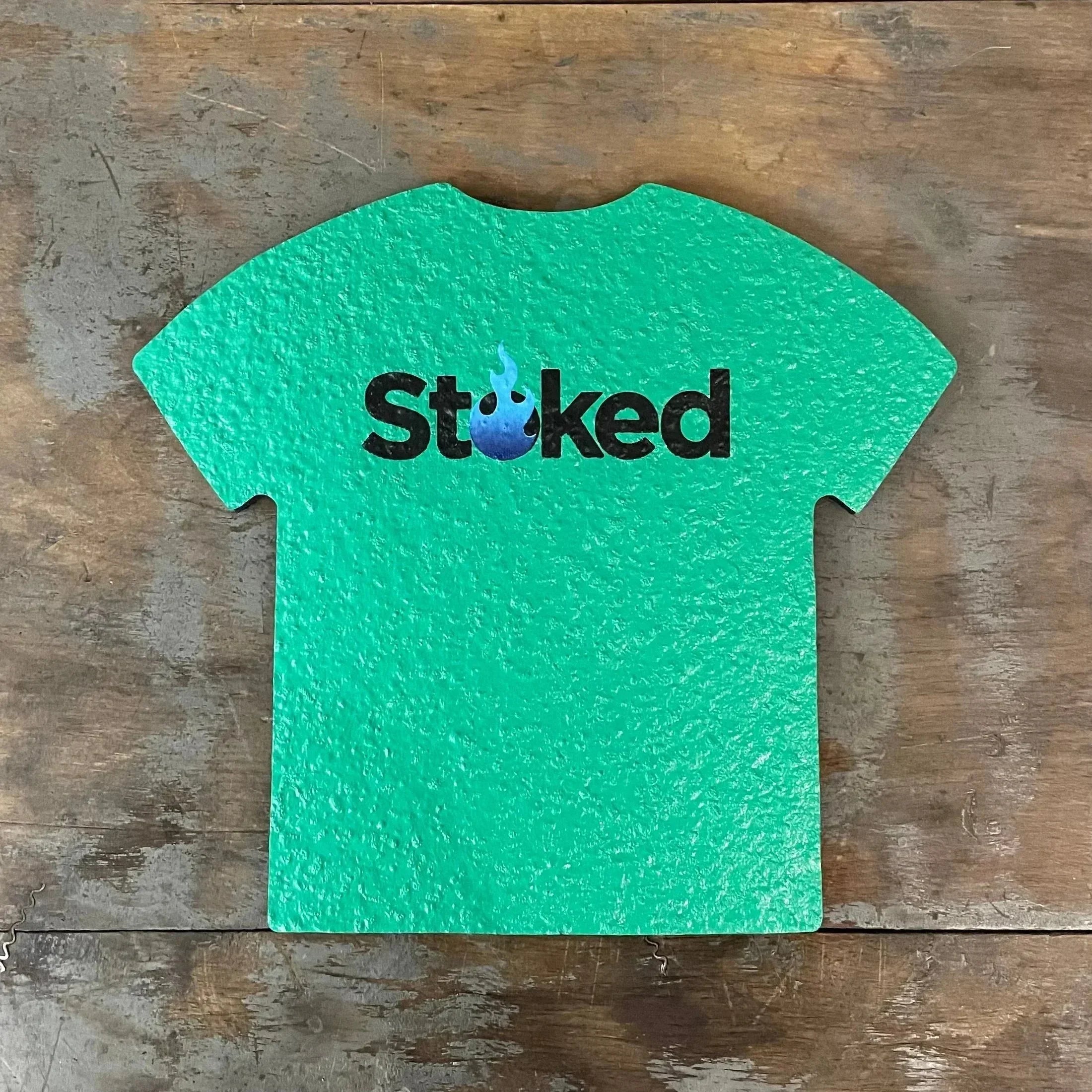 Green t-shirt shaped tray with 'Stoked' and blue flame logo on rustic wood background
