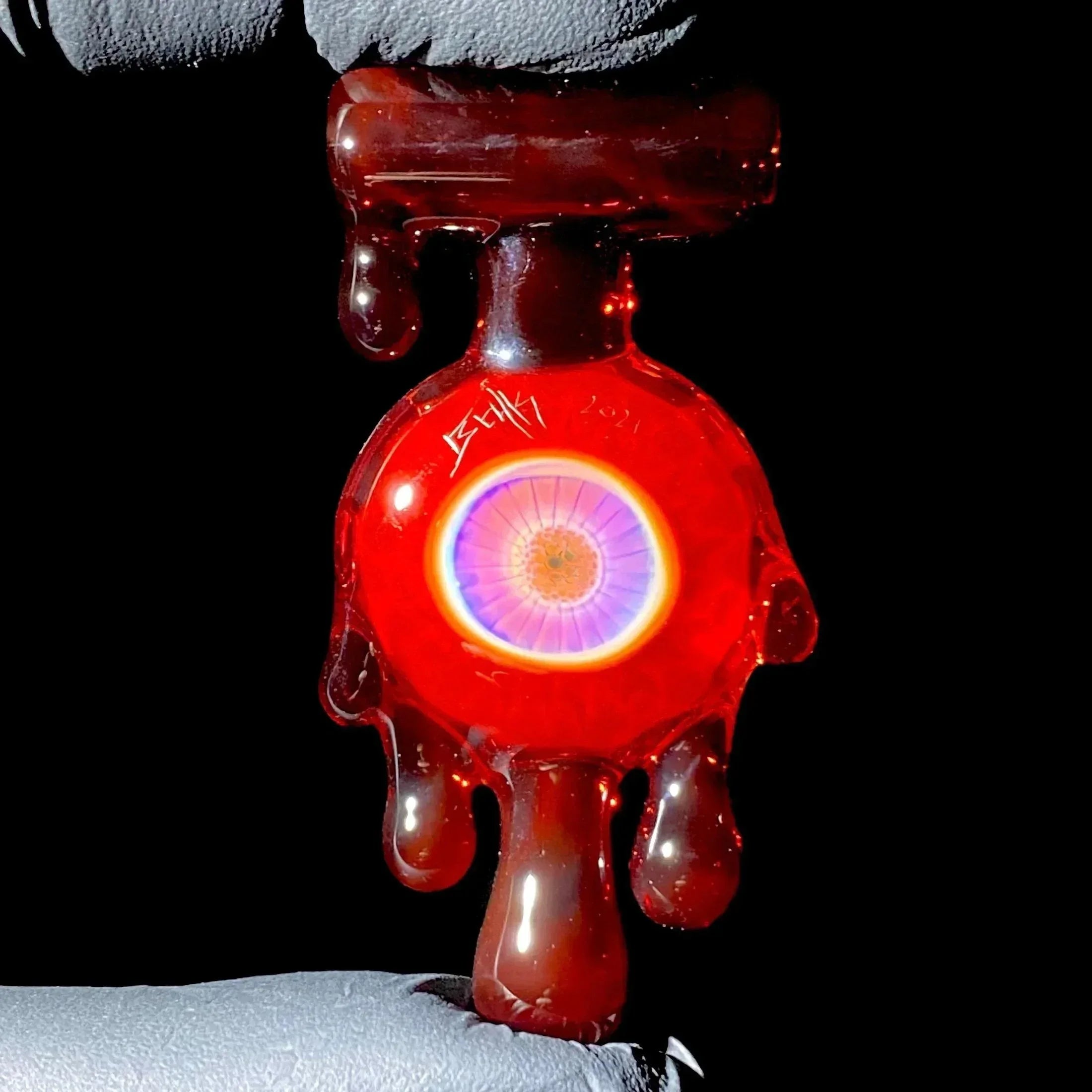 Hand holding red glass carb cap with vibrant eye design and drip accents