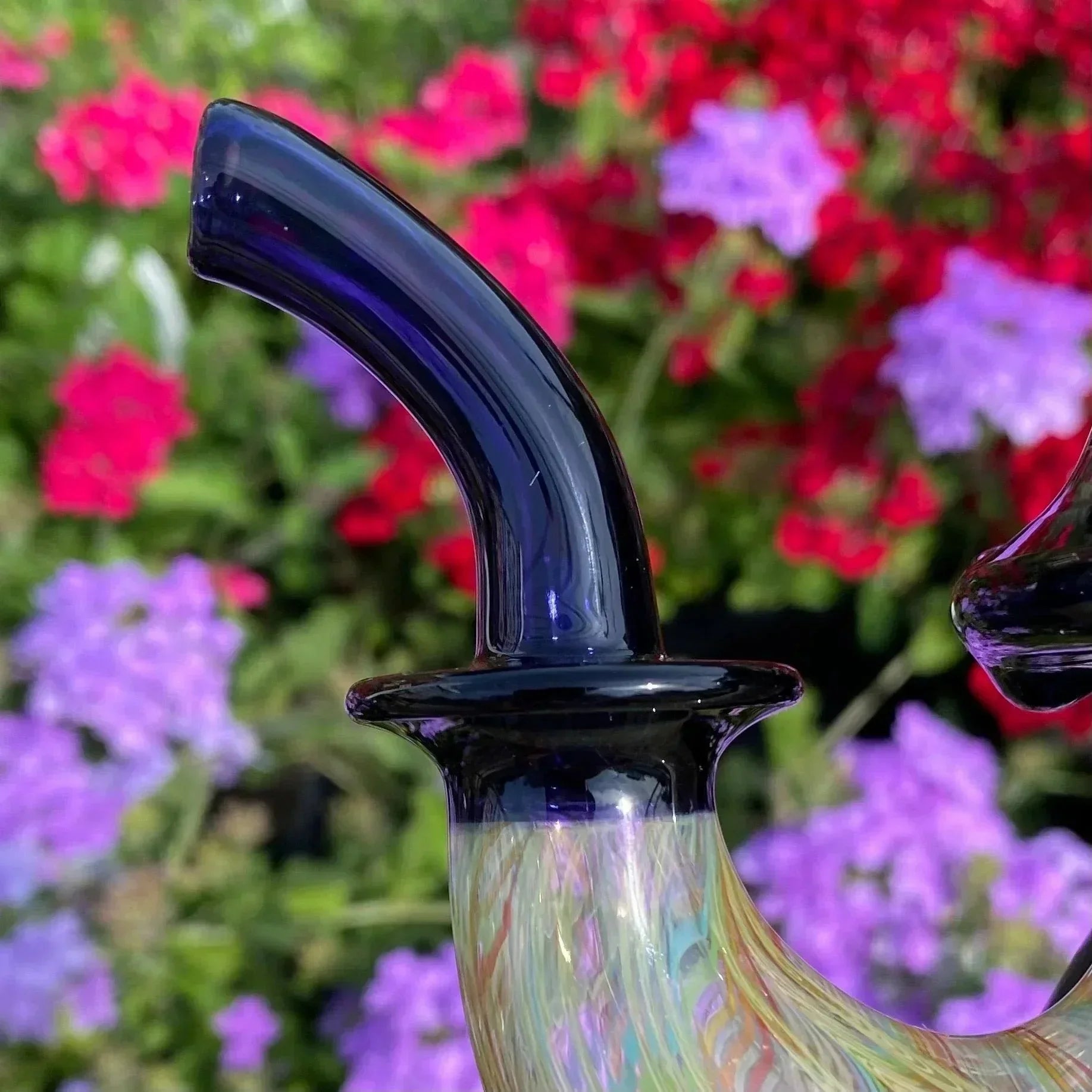 Close-up of a colorful glass pipe mouthpiece with floral background, artisan glasswork