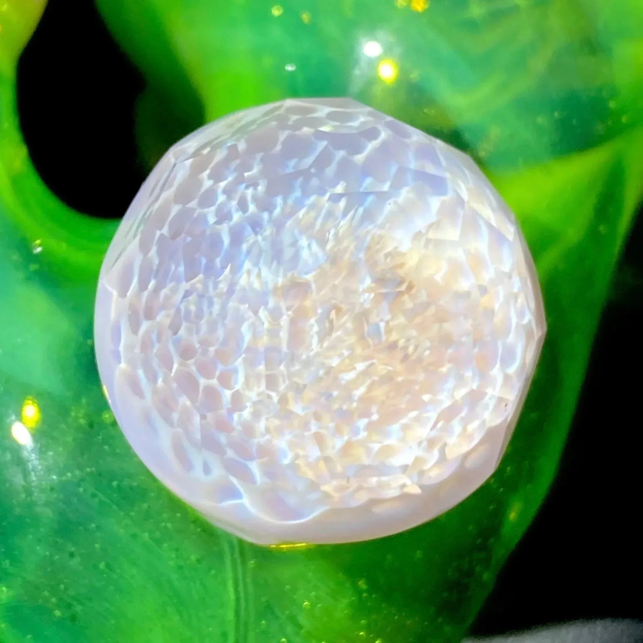 Close-up of iridescent textured glass marble on vibrant green background
