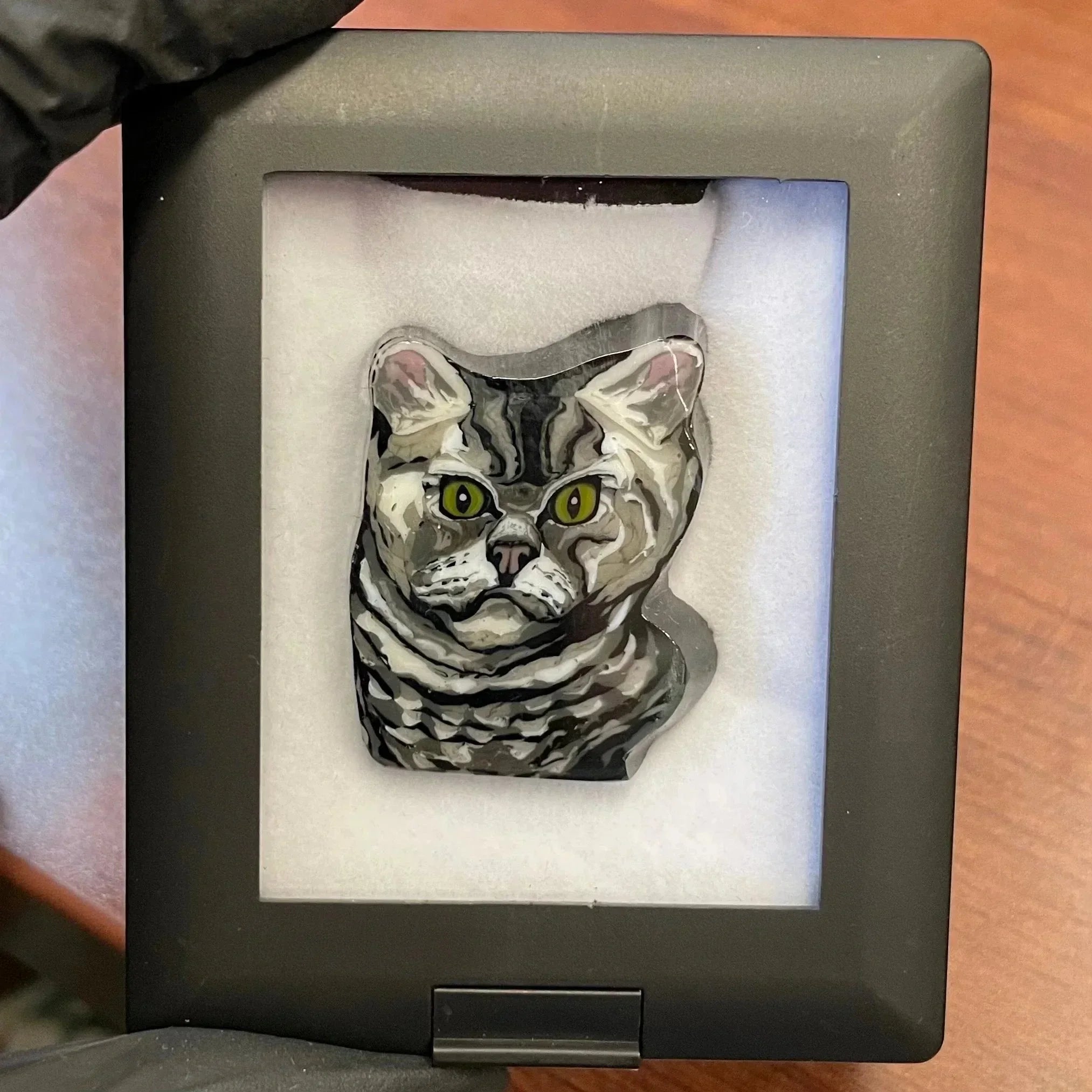Handmade glass pendant featuring a detailed gray tabby cat face with green eyes in a display case