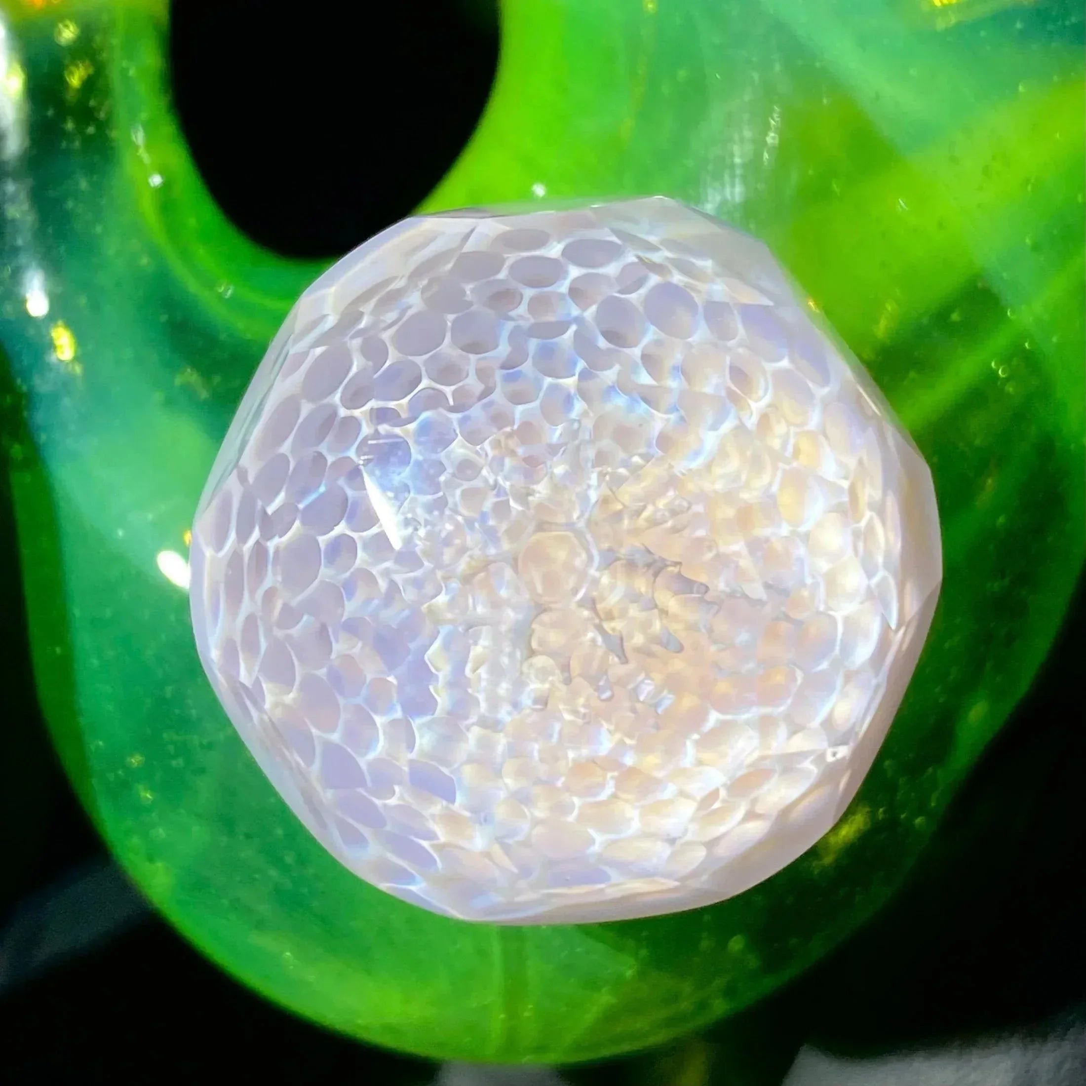 Iridescent honeycomb-patterned glass marble on vibrant green glass background