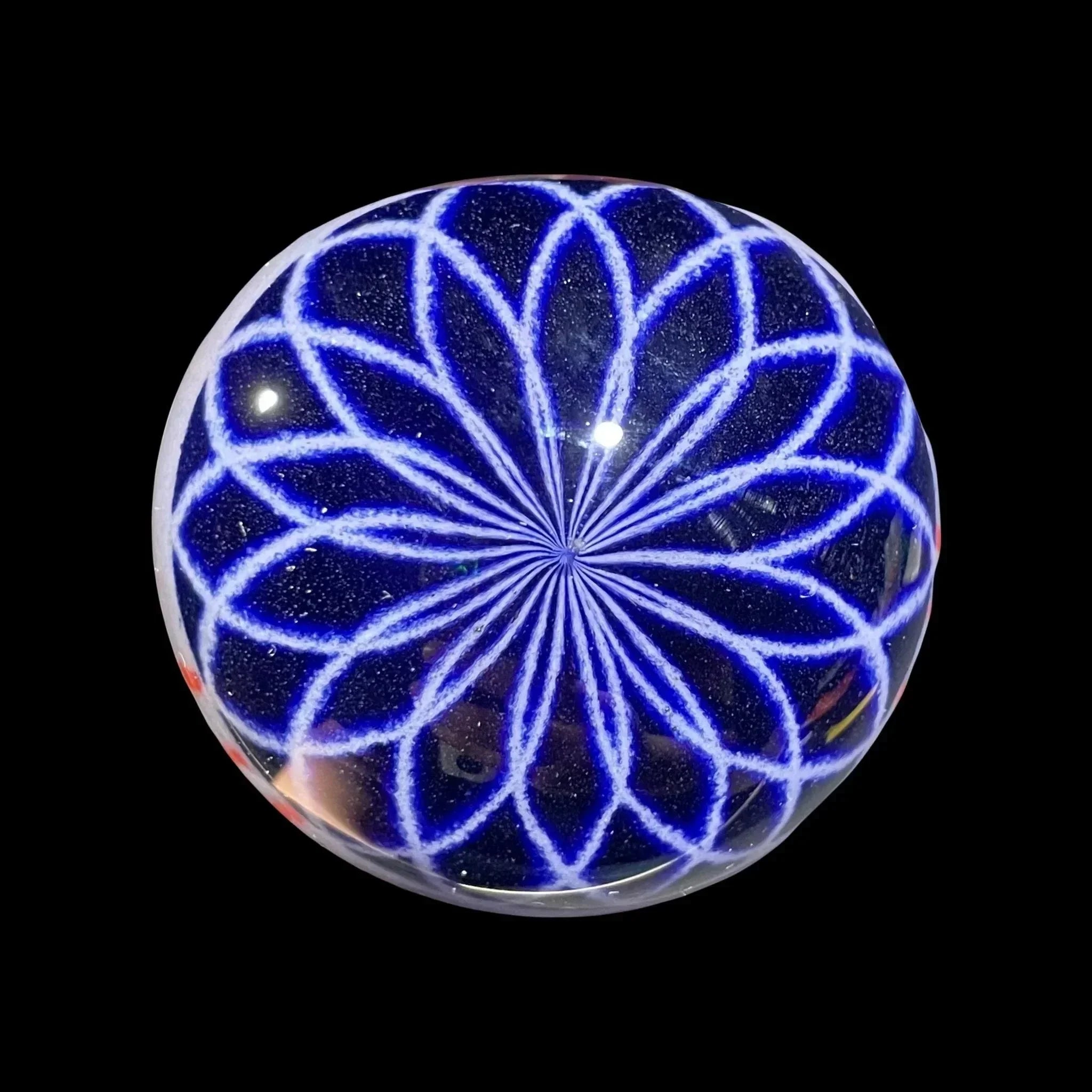 Hand-blown glass marble with blue geometric flower pattern on black background