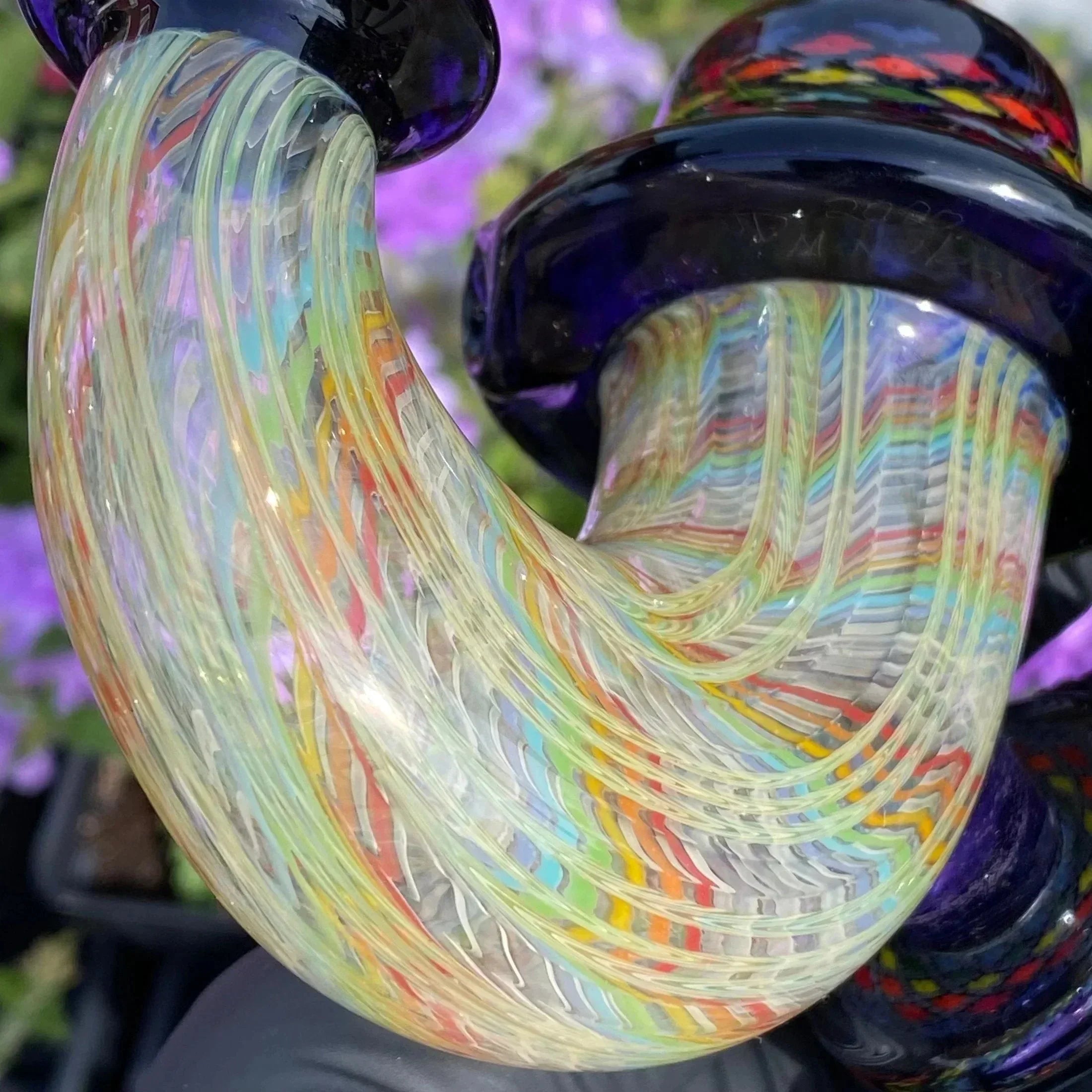 Close-up of intricate heady glass pipe with colorful swirled patterns, outdoor background