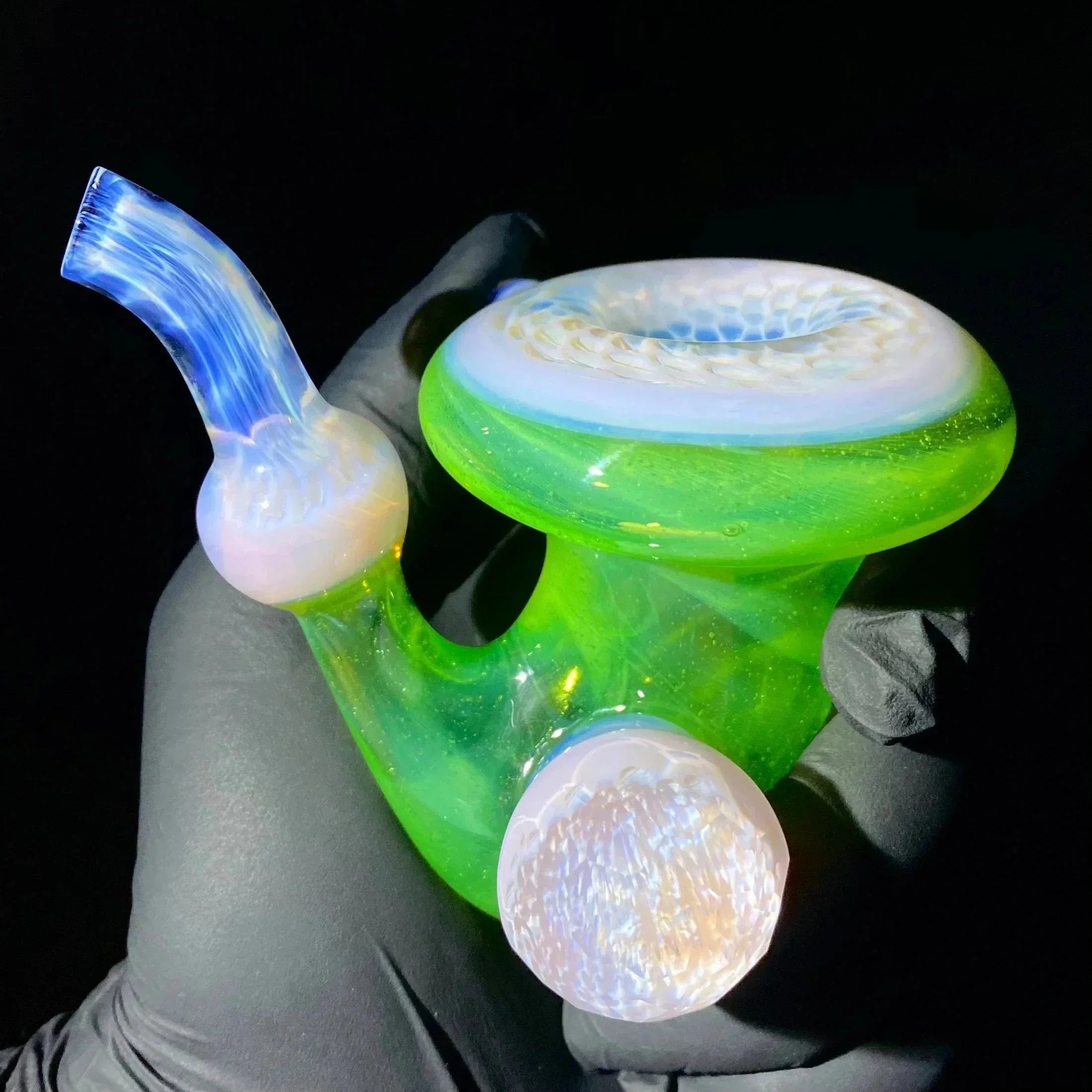 Hand holding a vibrant green and blue heady glass pipe with intricate textured details