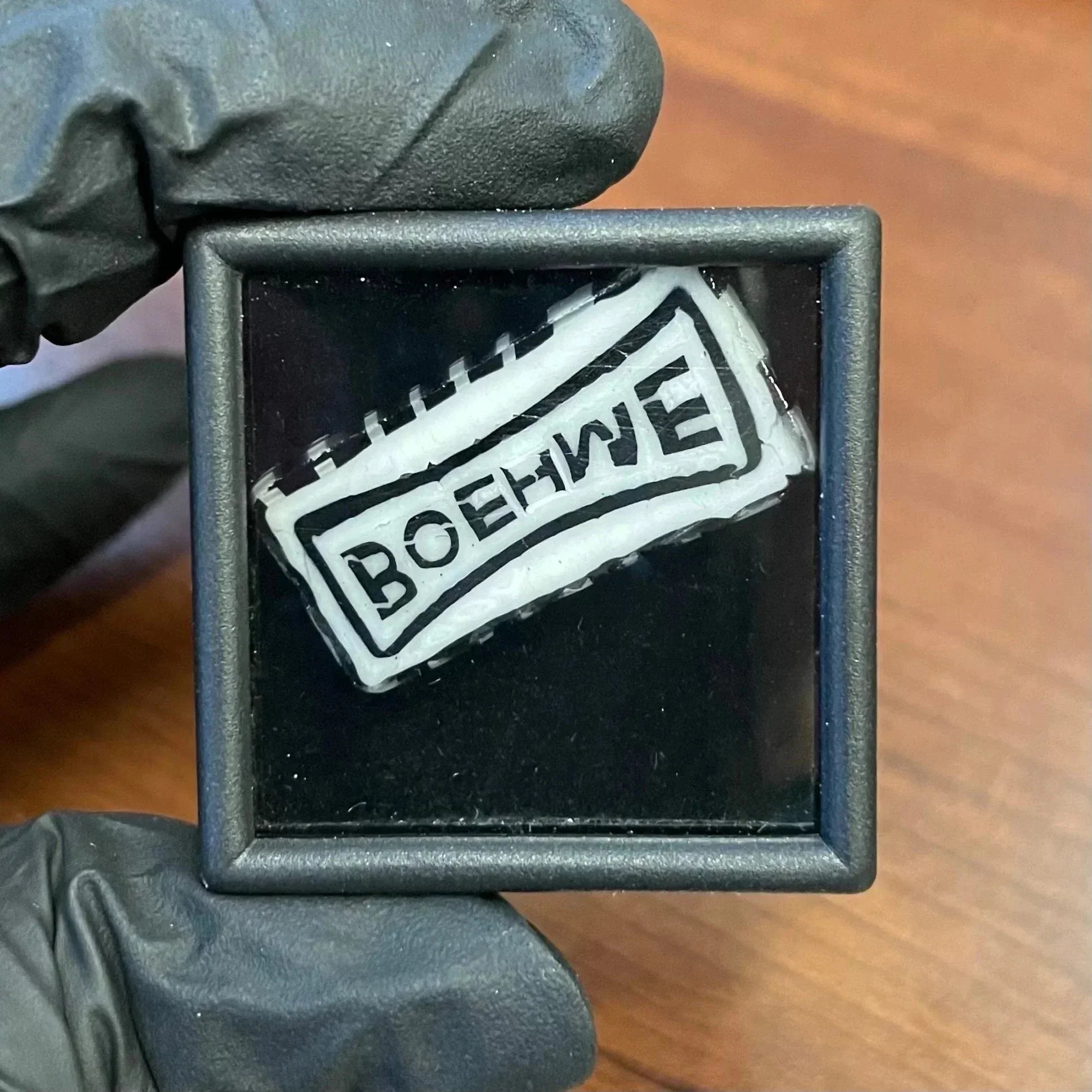 Glass art encased in a display box, white and black cane with BOEHWE text, wood background