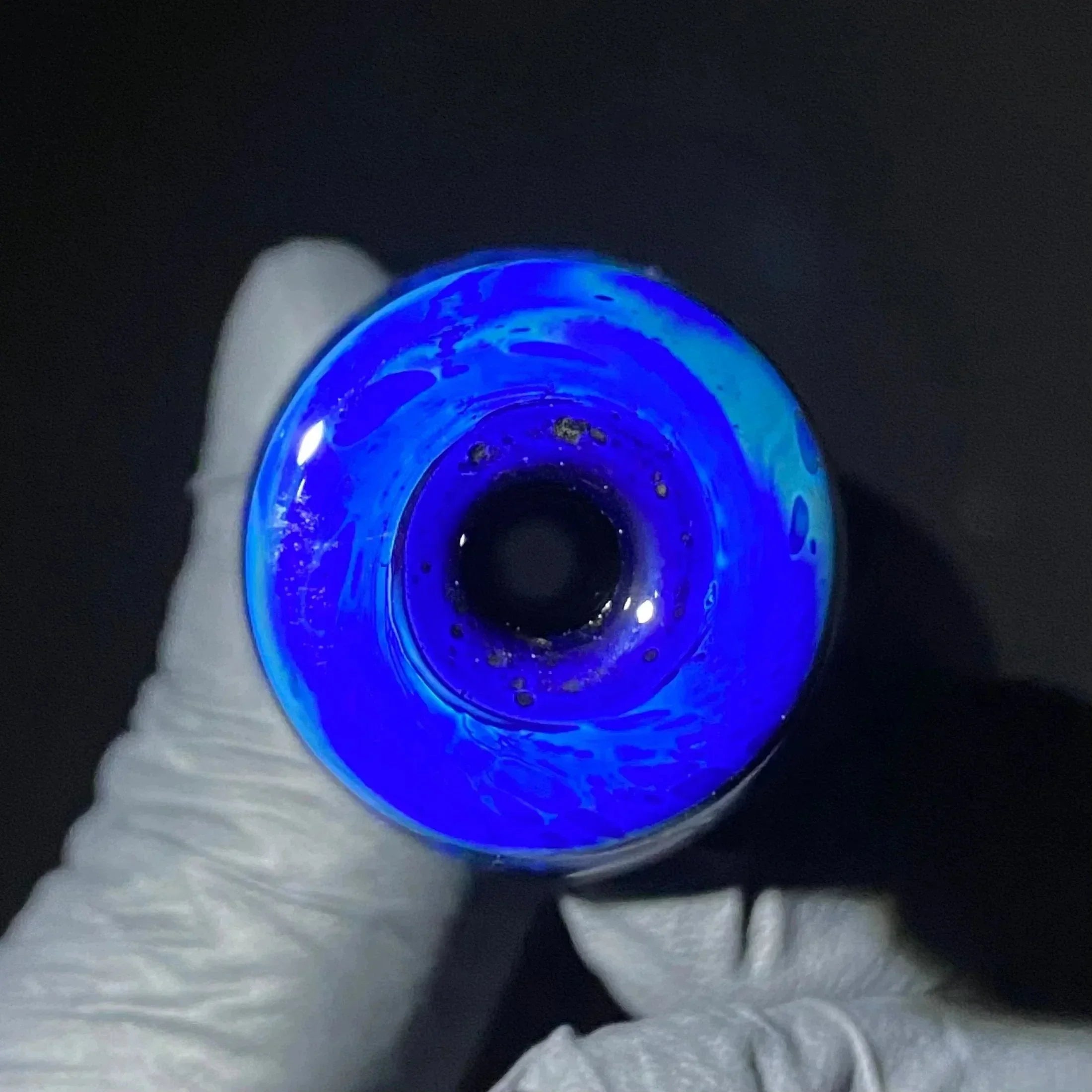 Close-up of blue glass pipe bowl with swirling patterns, held in gloved hand