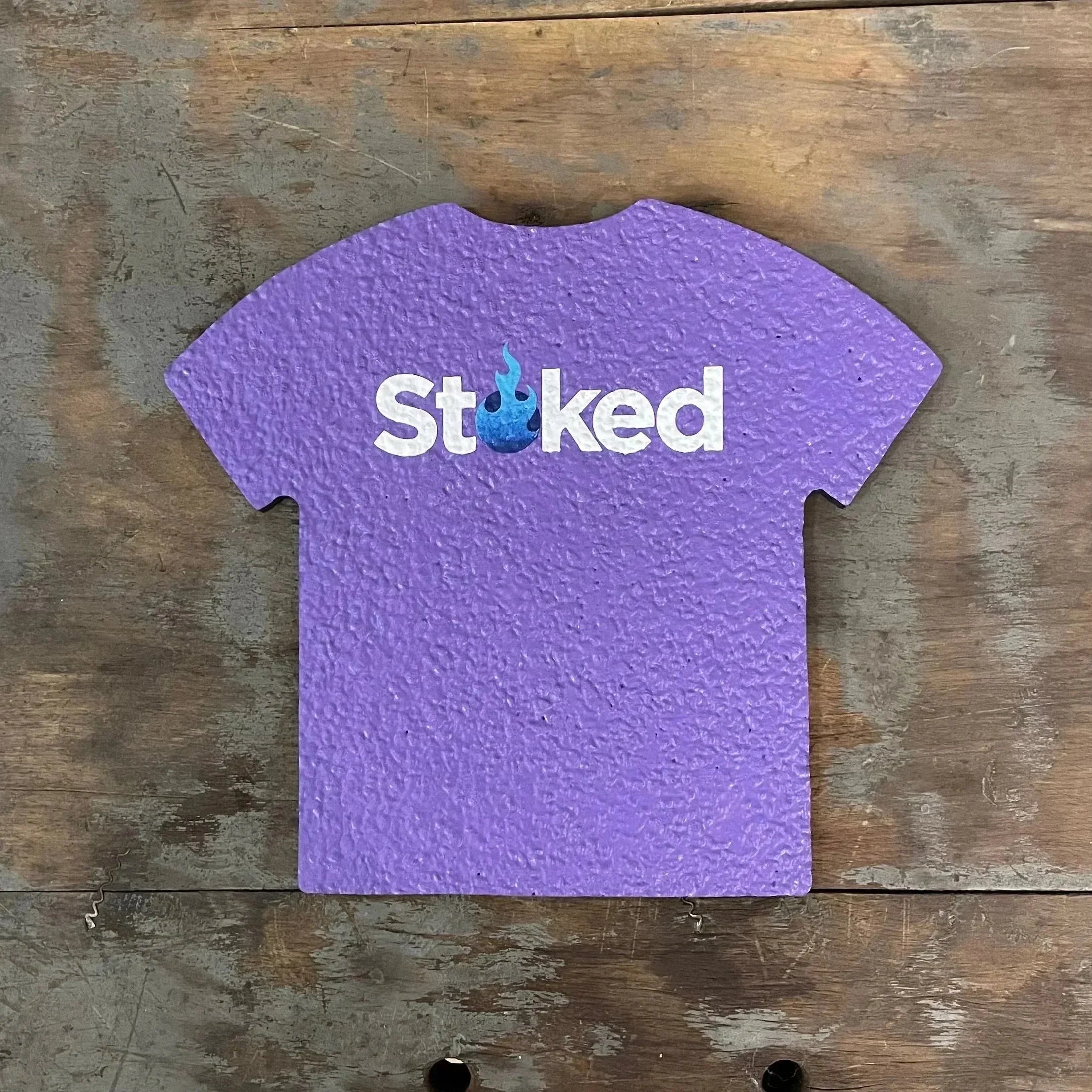 Purple textured t-shirt shaped tray with 'Stoked' and blue flame graphic on wood background