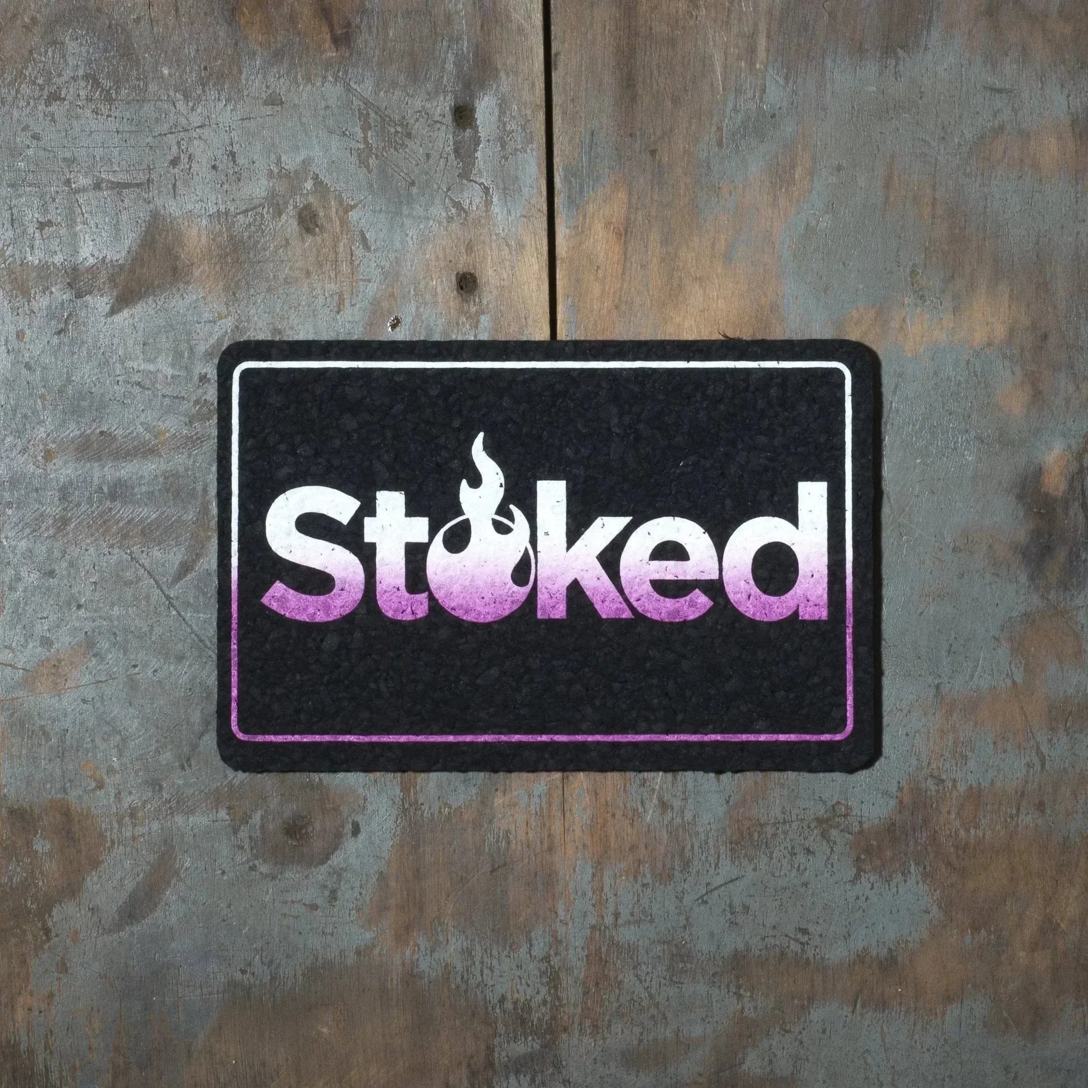 Stoked logo mat with purple gradient and flame design on rustic wood background