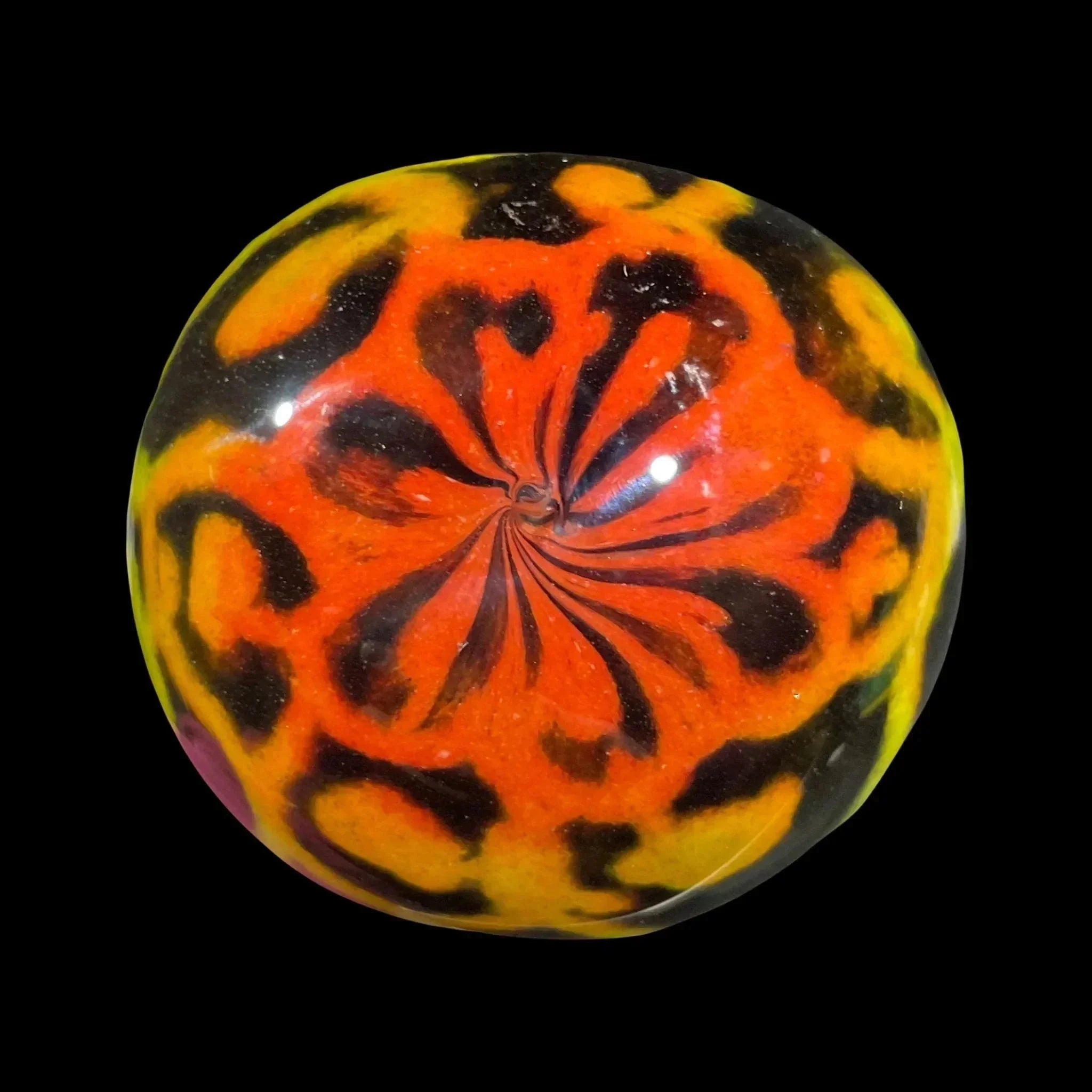 Hand-blown glass marble with vibrant orange, yellow, and black swirl design on black background