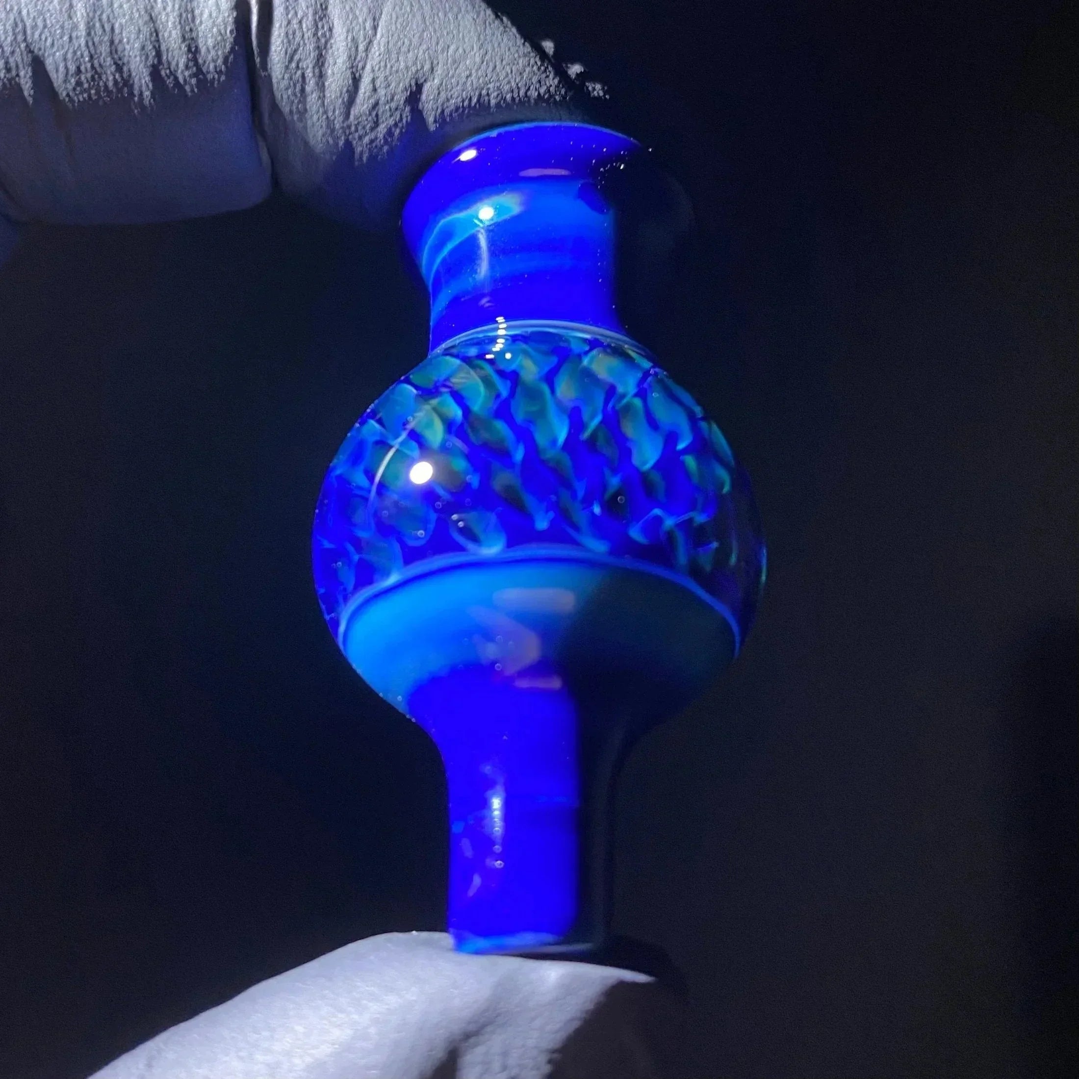 Hand holding blue glass carb cap with intricate patterns for dab rig or concentrate setup