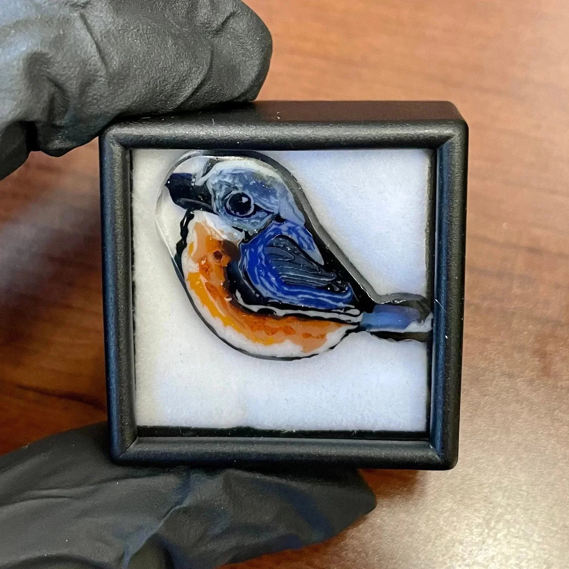 Handmade glass art bird pendant with blue and orange details in a display box