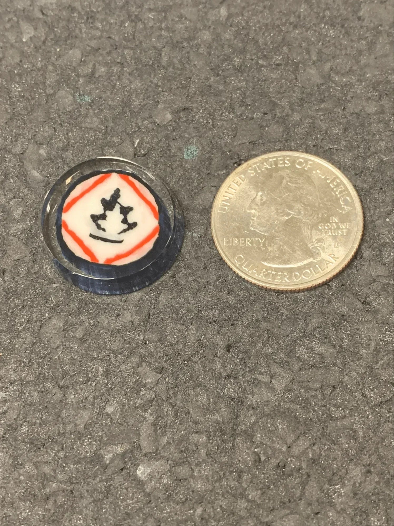 Small glass accessory with red and black design next to quarter for scale