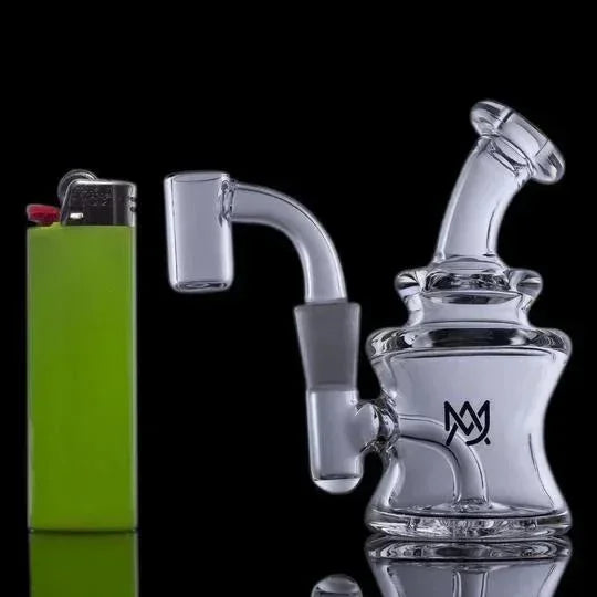 Mini clear glass dab rig with quartz banger next to green lighter on black background