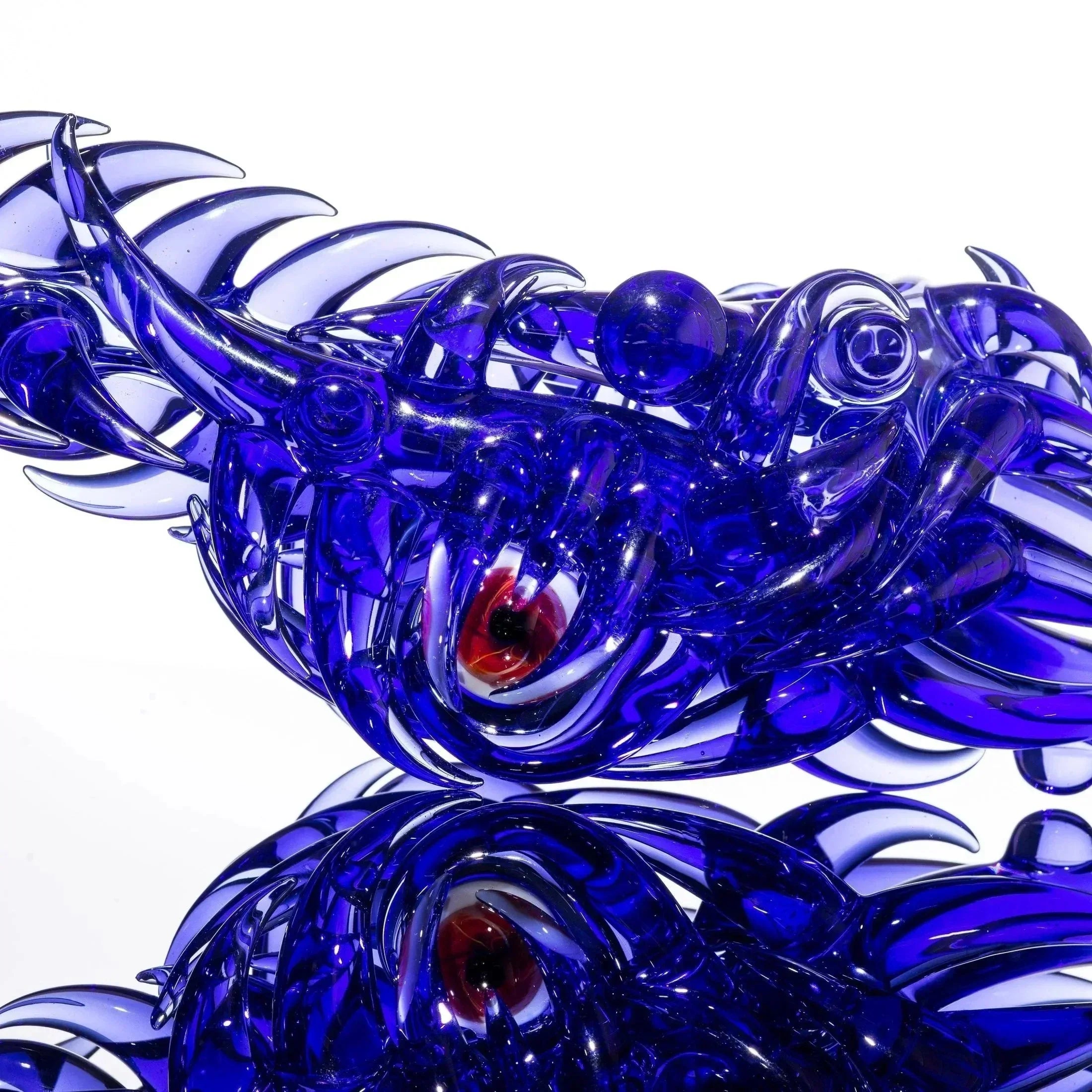 Vivid blue heady glass sculpture with swirling tentacles and red eye detail, reflective surface