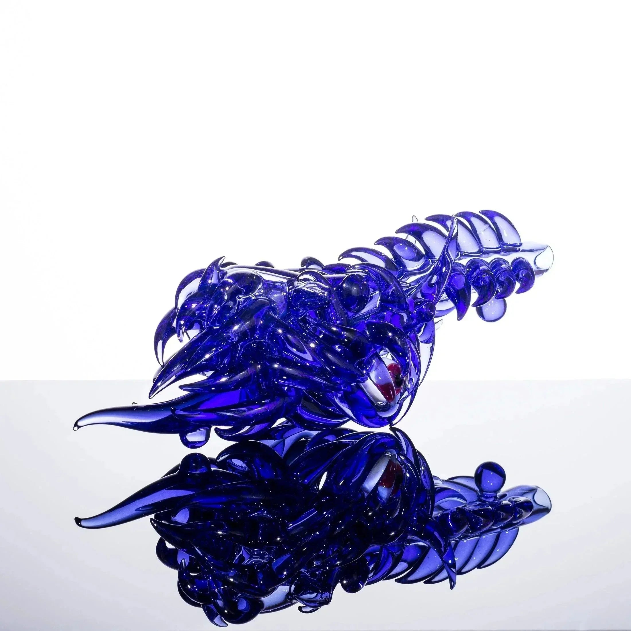 Vibrant blue heady glass dragon sculpture with intricate scales and red eyes, displayed on reflective surface