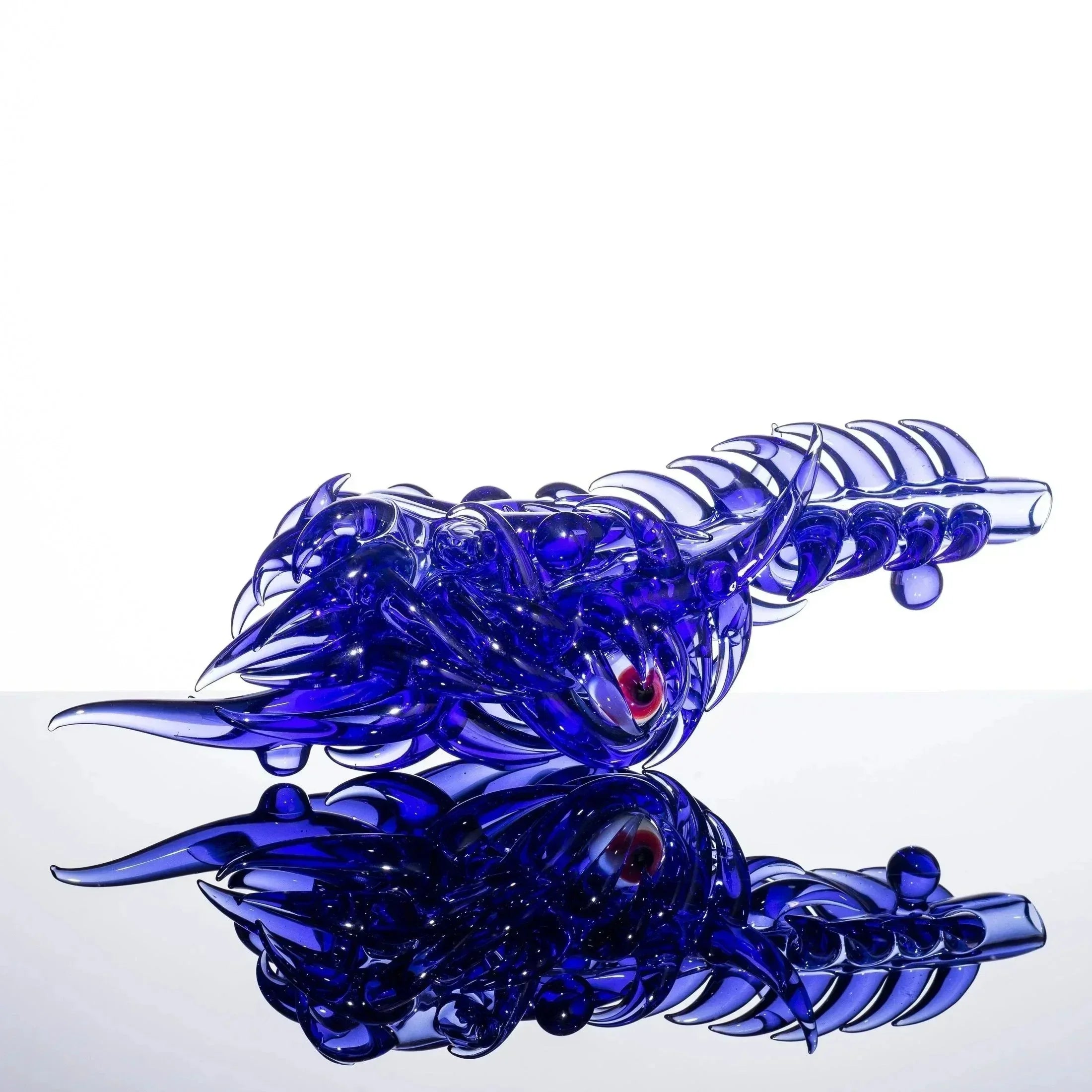 Blue glass dragon sculpture with red eye, intricate scales, and reflective surface, showcasing heady glass artistry.