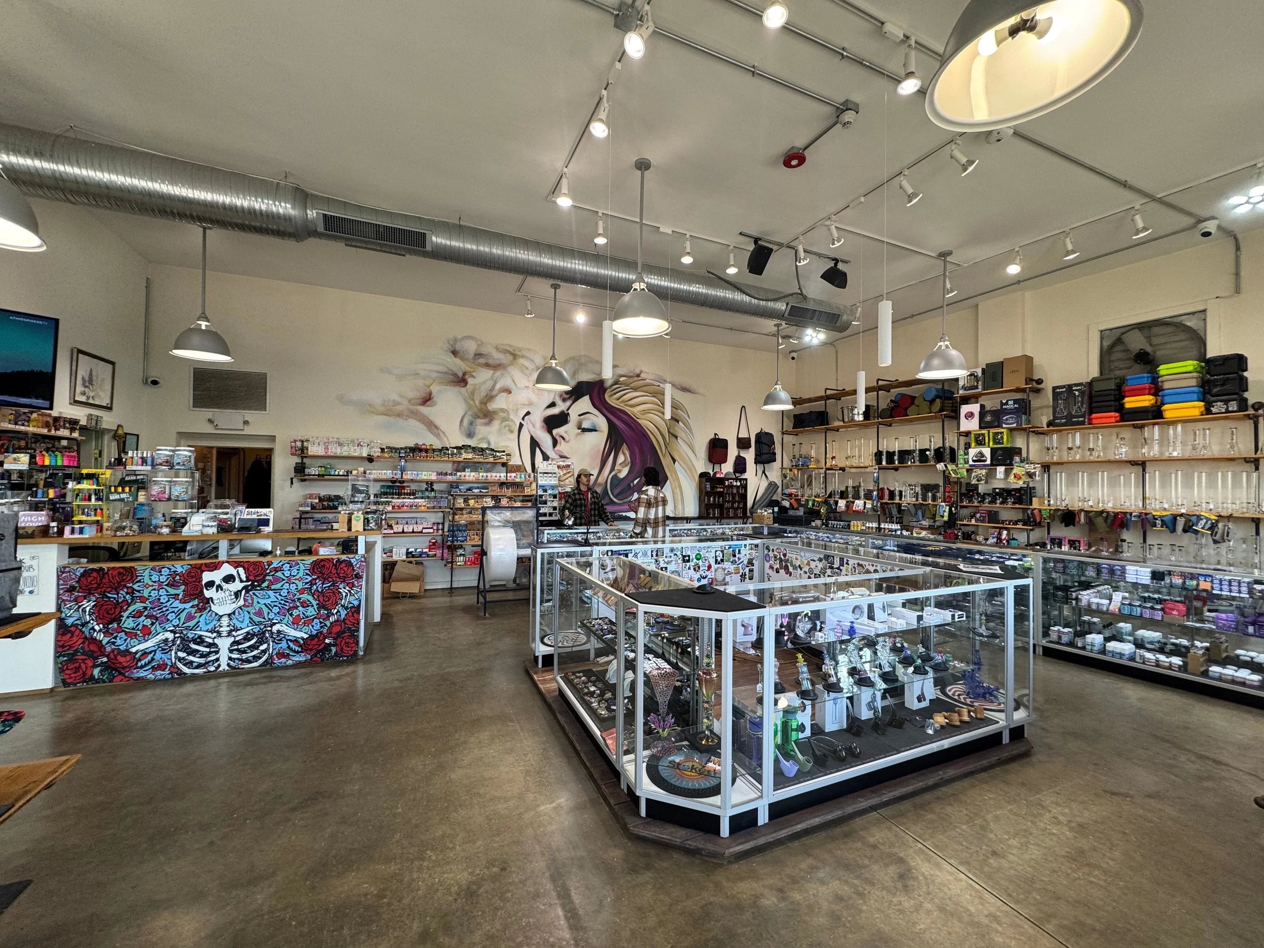 Modern smoke shop interior with glass display cases, smoking accessories, colorful mural and pipes.