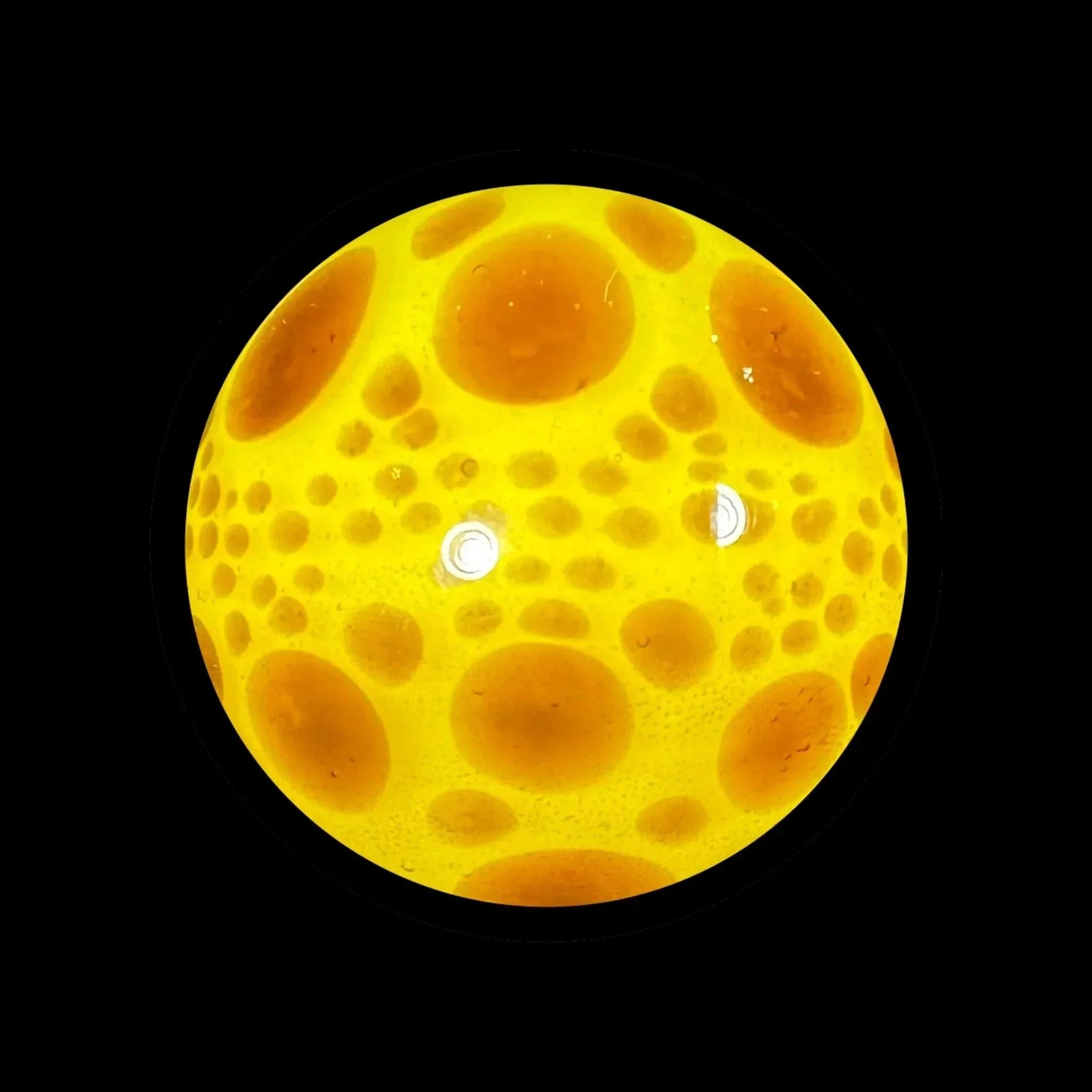 Yellow glass marble with orange bubble-like spots on a black background