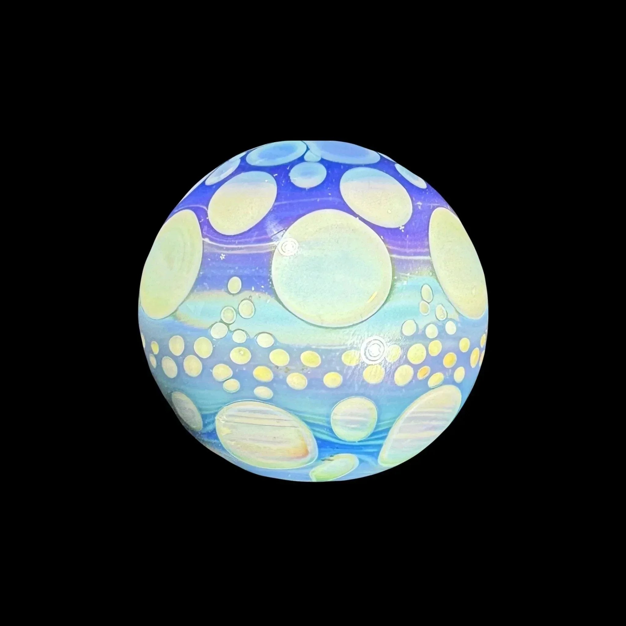 Colorful glass marble with blue and yellow bubble patterns on a black background