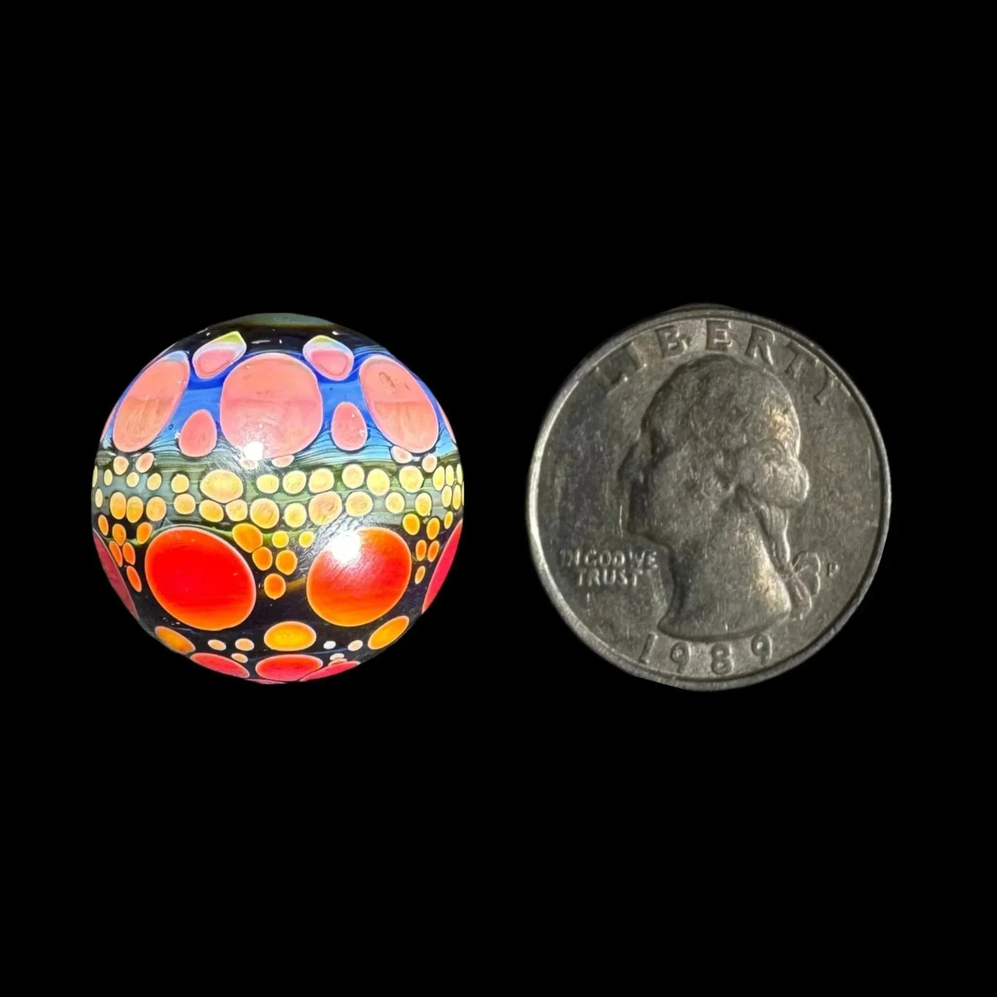 Colorful glass marble with dotted pattern next to a US quarter for size comparison