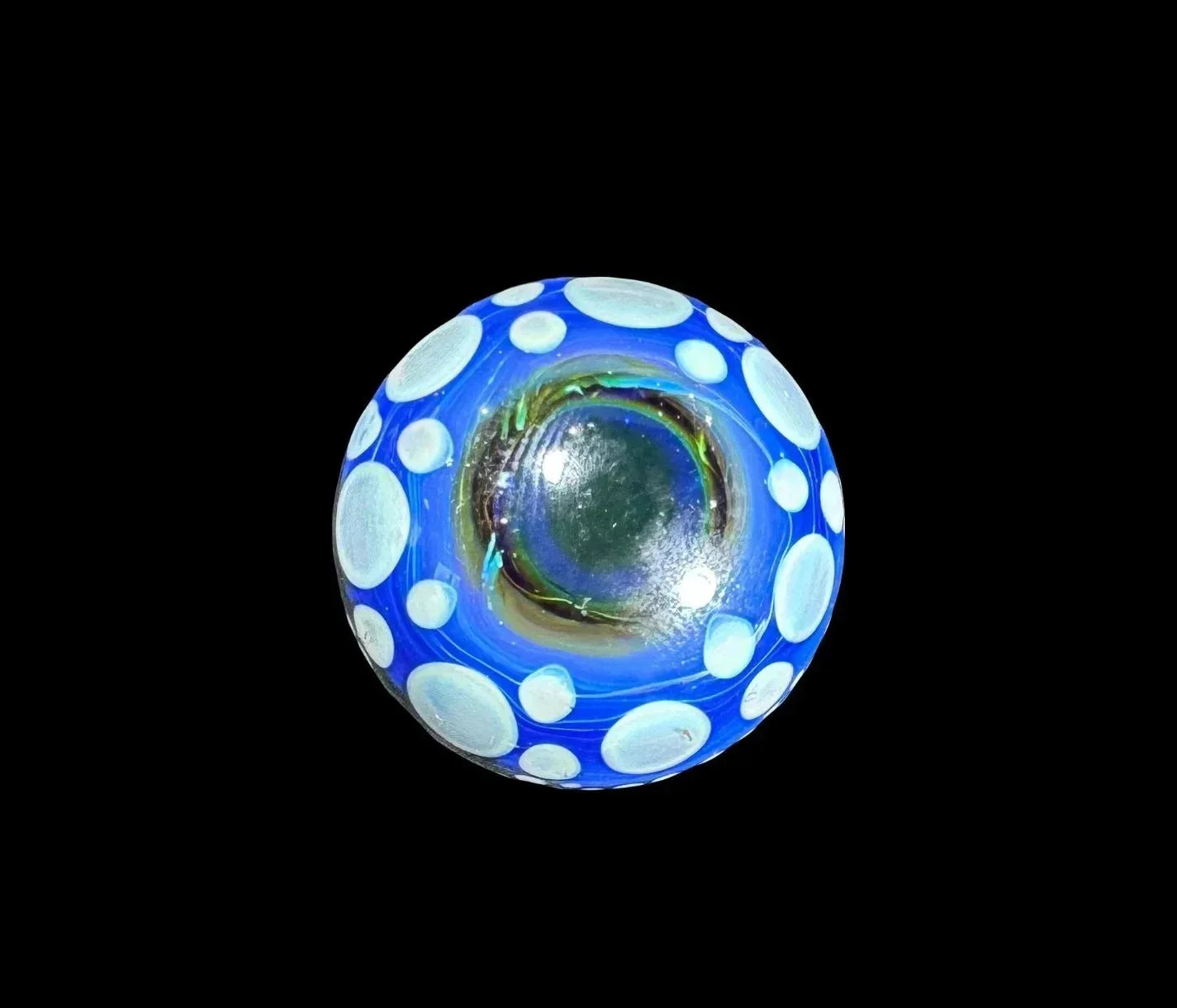Blue glass marble with white polka dots and iridescent center on black background