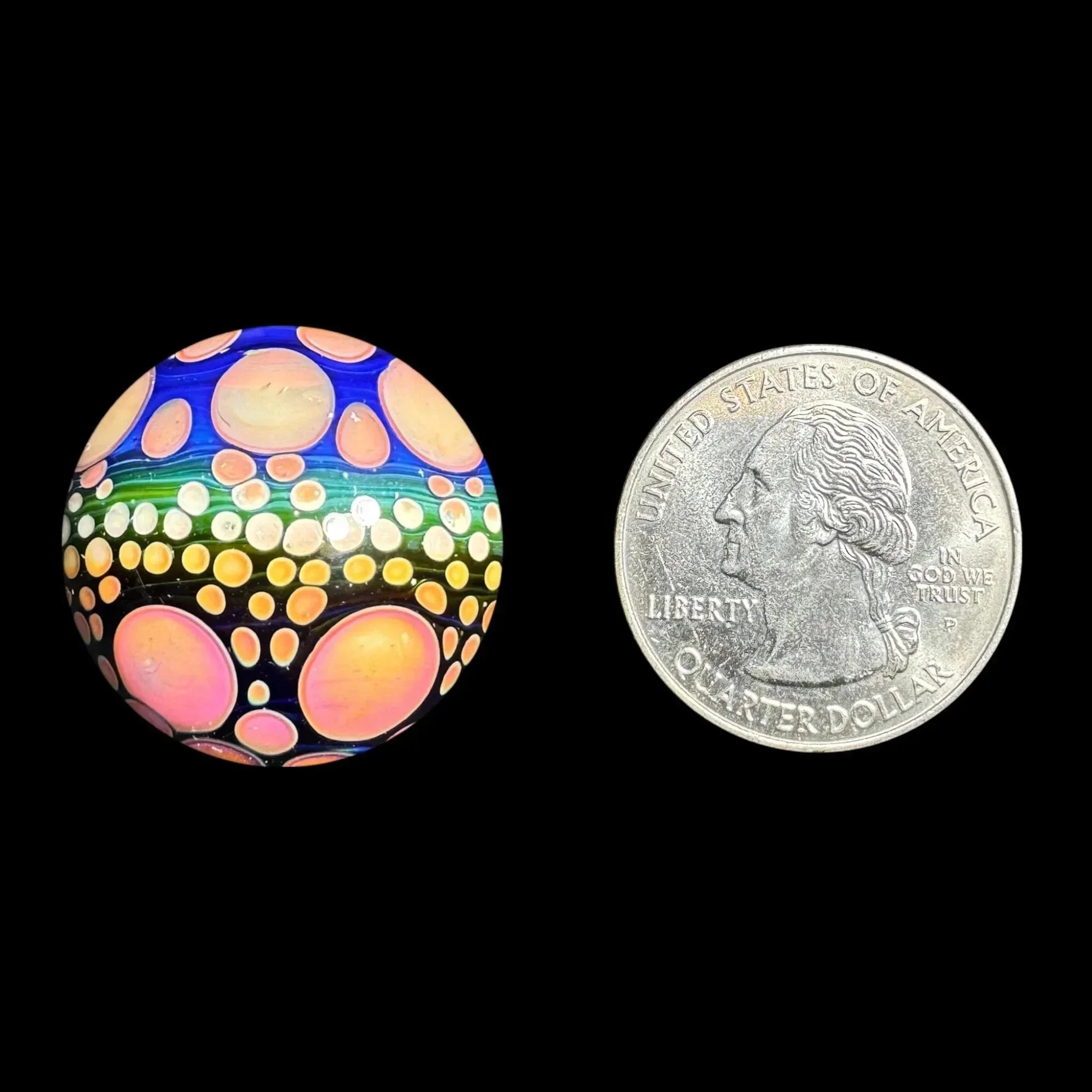 Colorful glass marble with dot pattern next to US quarter for size comparison
