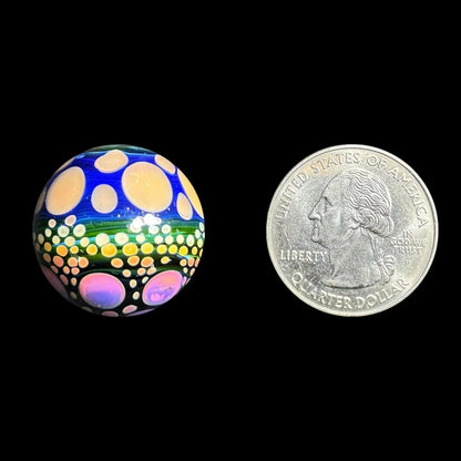 Colorful glass marble with polka dot design next to a US quarter for size comparison
