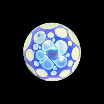 Handcrafted blue glass marble with yellow dots and abstract patterns on black background